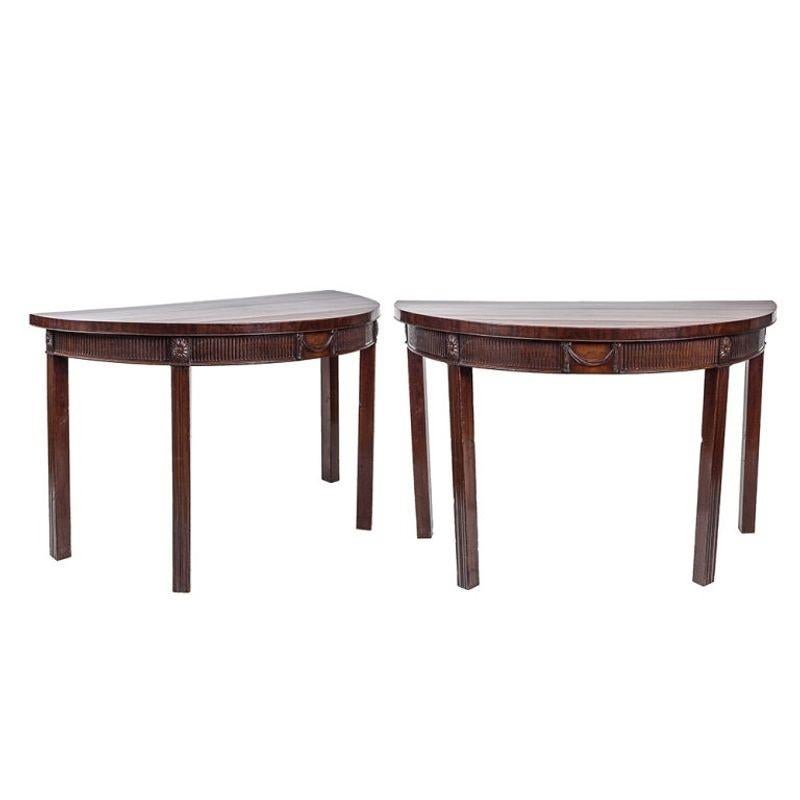 Pair of Mahogany Demilune tables. The frieze of each is fluted with a central carved swag and carved sunflowers above each of the four Marlborough legs.