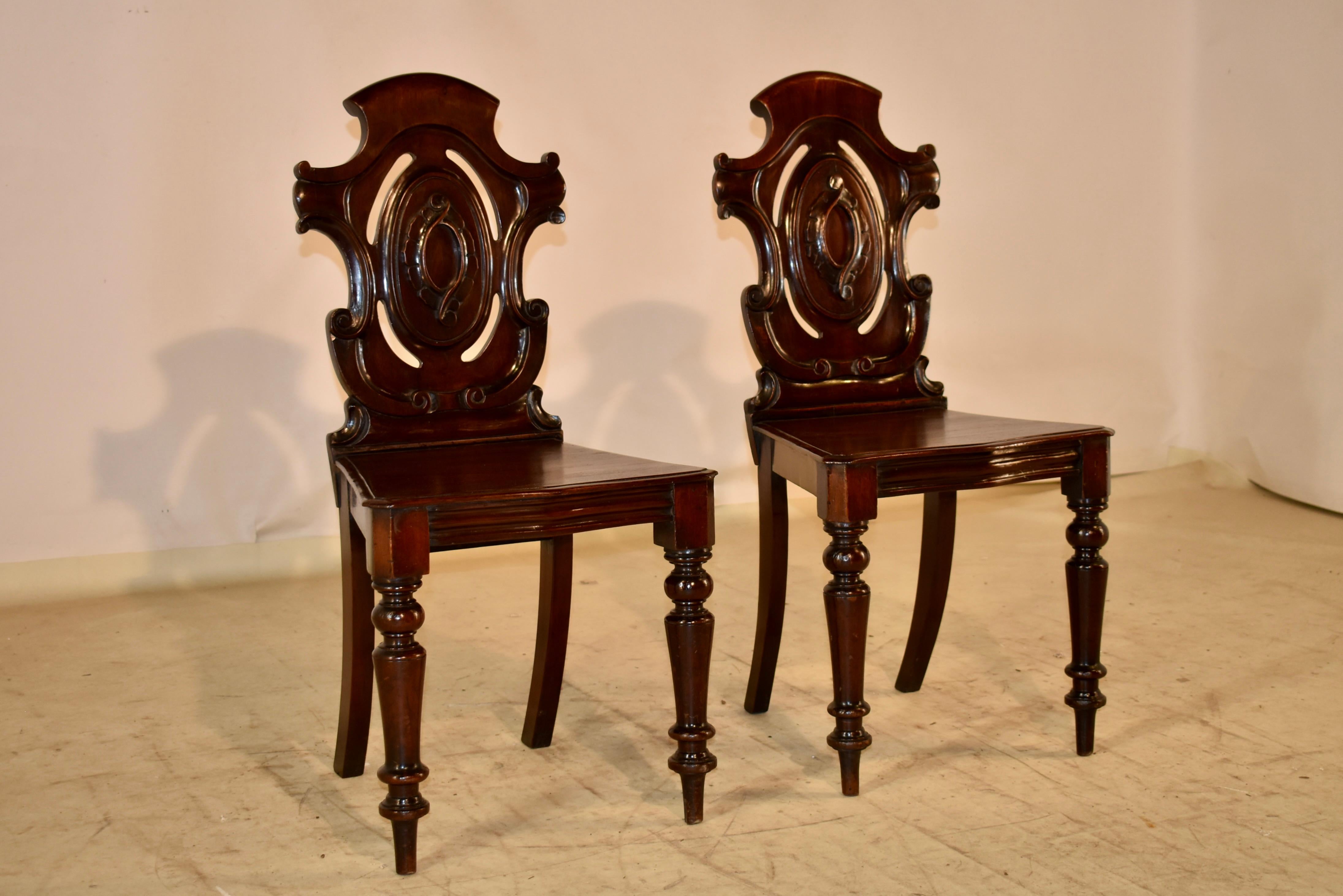 Pair of 19th century mahogany hall chairs from England.  The backs are in the shape of shields, which are pierced and have a central lozenge in the back with carved decoration.  The seats are also shaped like shields and the chairs are supported on