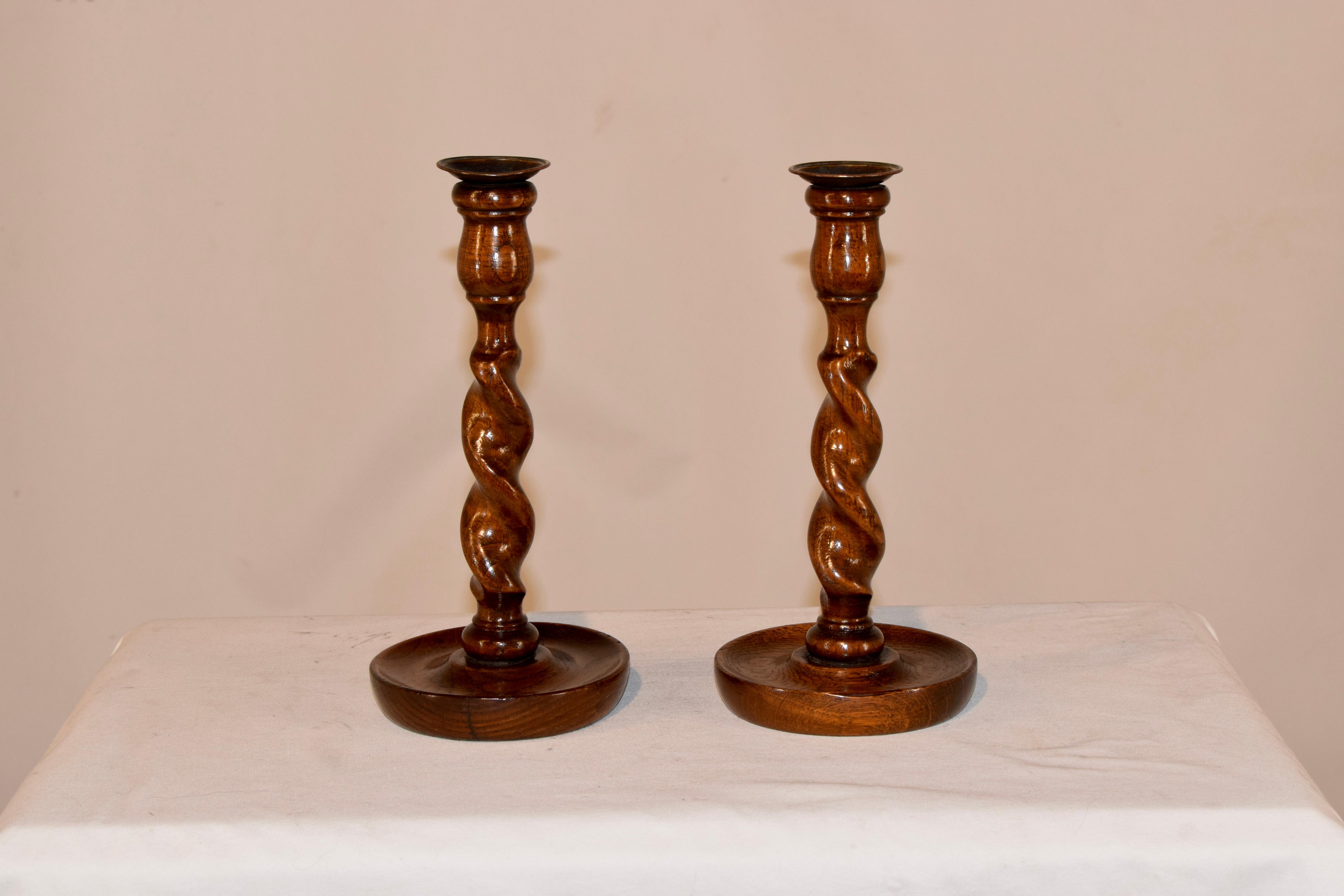 Pair of late 19th century English oak candlesticks with tulip turned candle cups, which retain the original brass candle cups over hand turned barley twist stems and supported on hand turned dish shaped bases.