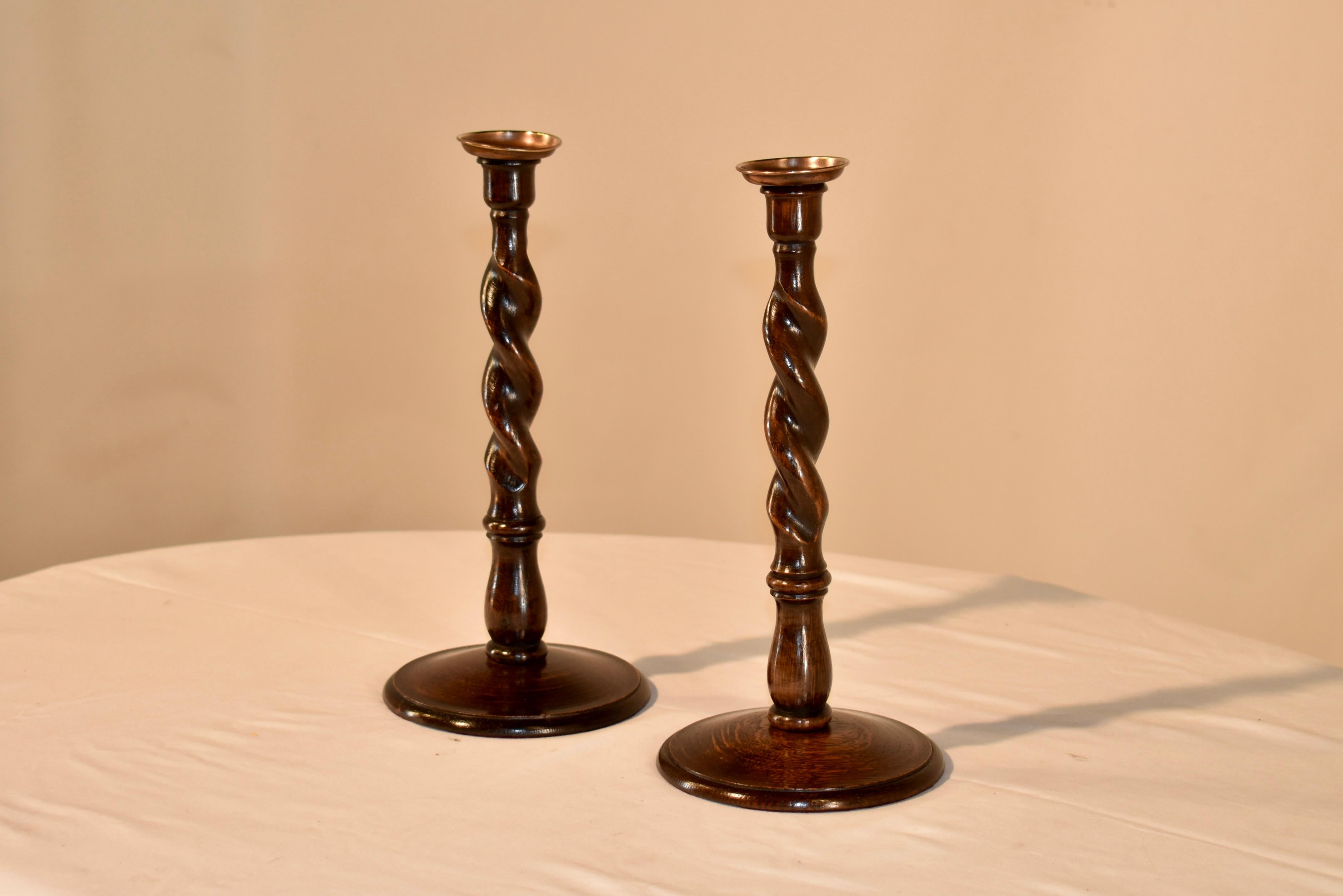 Pair of late 19th century oak candlesticks from England with hand turned candle cups supported on top of barley twist stems and resting on hand turned bases, which have beveled edges along the bases.