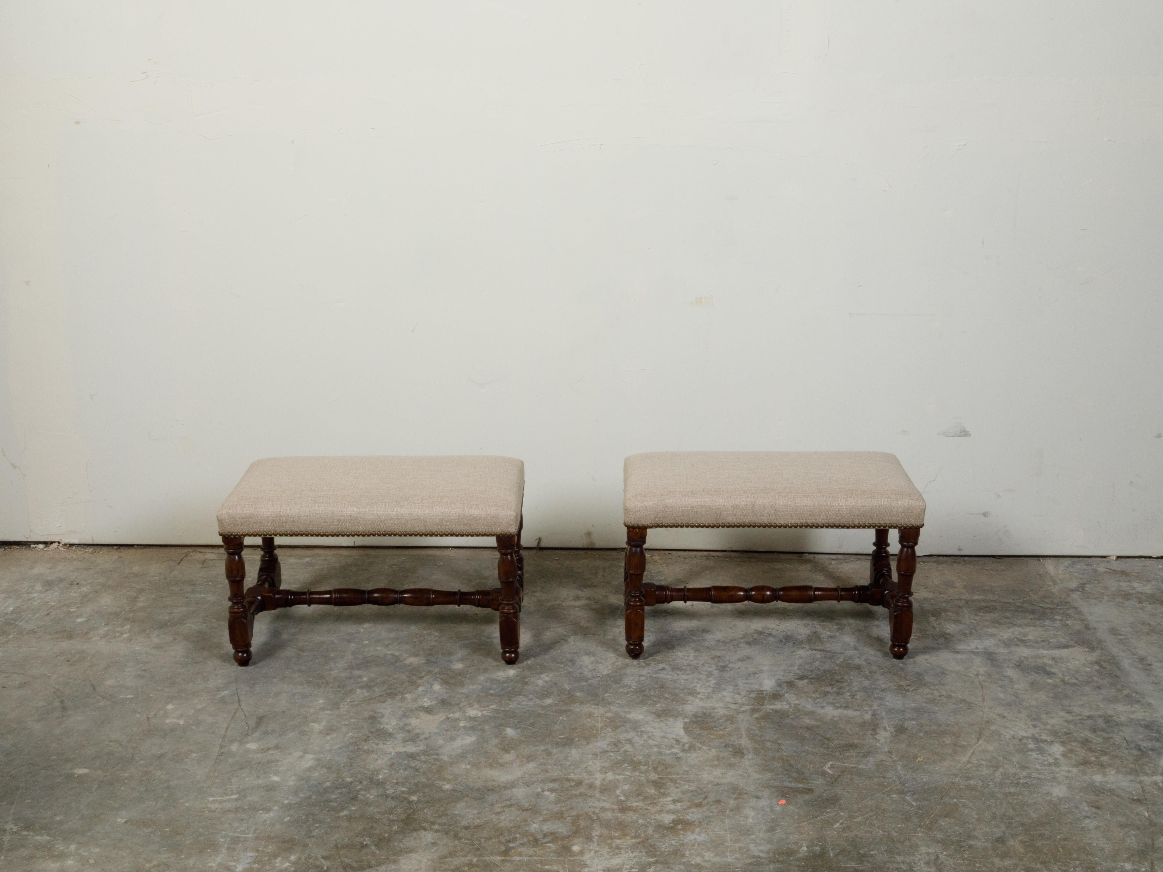A pair of English oak benches from the 19th century, with turned bases, new upholstery and brass nail heads. Created in England during the 19th century, each of this pair of oak benches features a rectangular top newly reupholstered with a neutral