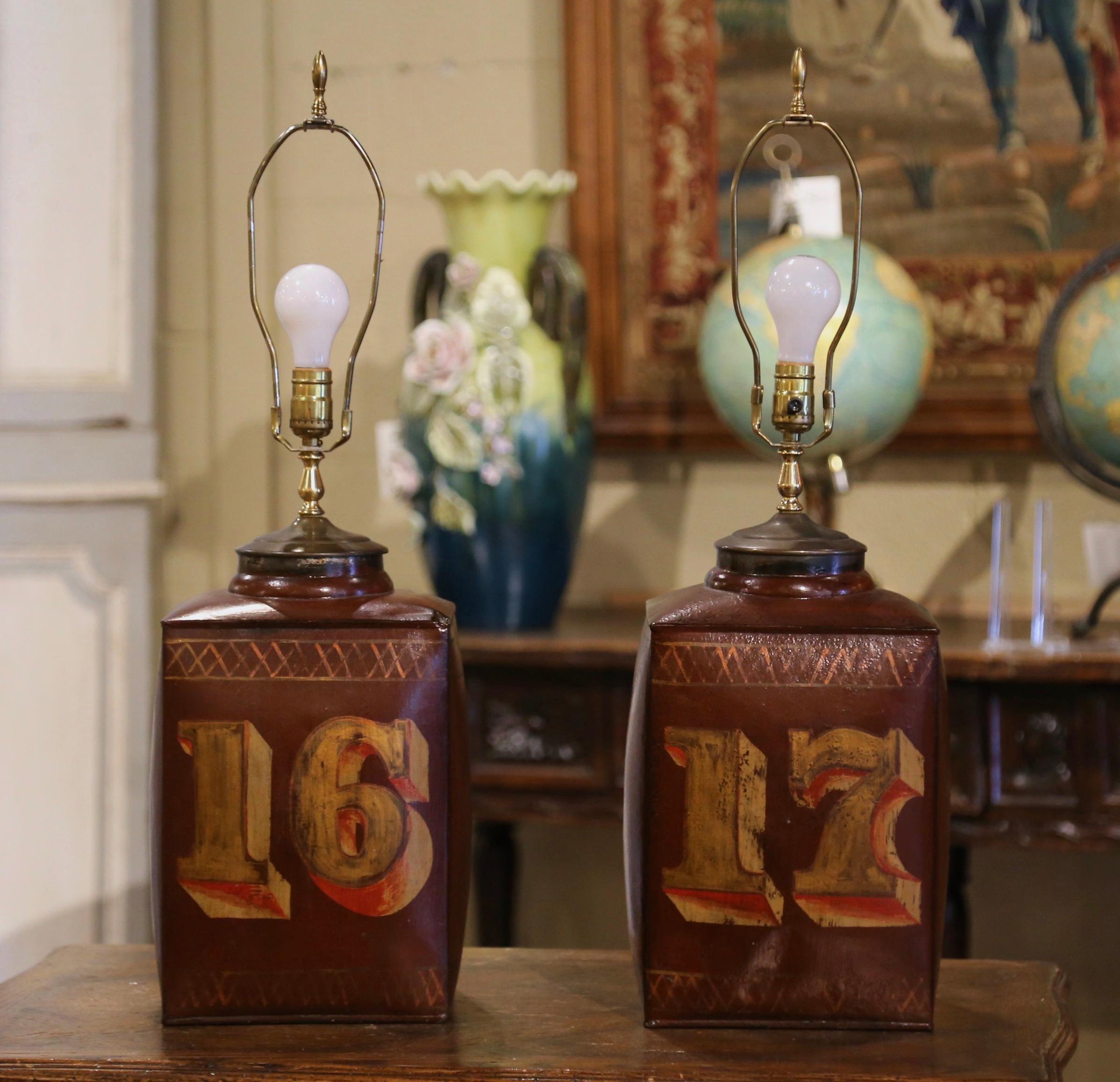 Decorate bedside tables in a master bedroom, or side tables in a living room with this elegant pair of antique canister lamps. Created in England, circa 1890 and made of tole, each large tea box features a colorful hand painted number with the