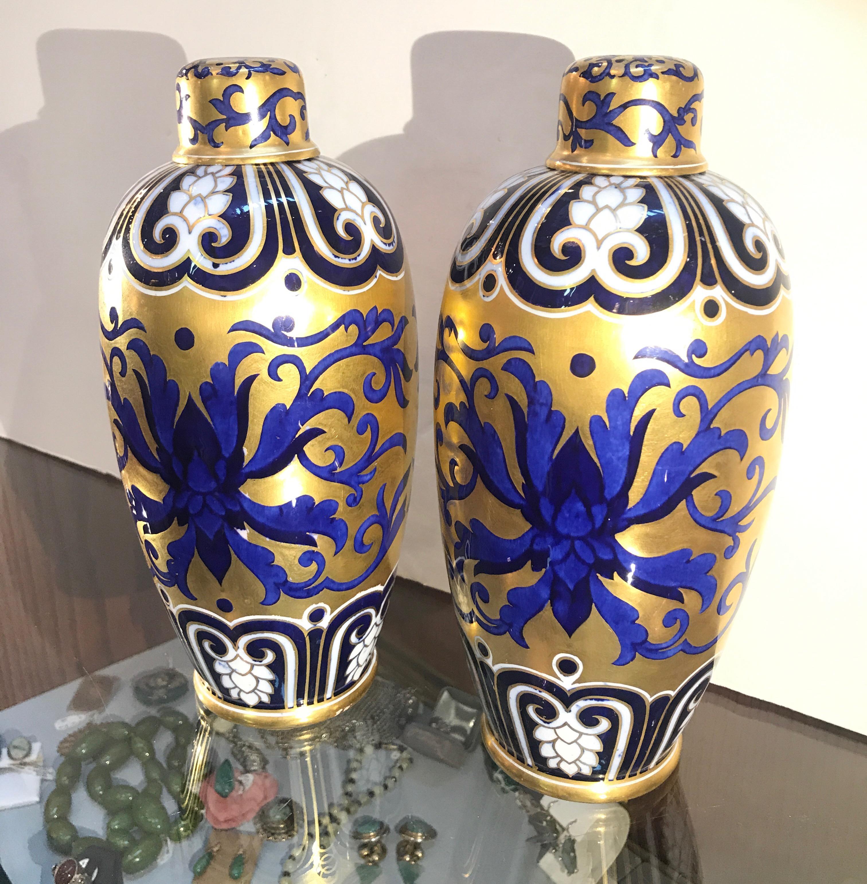 A stunning pair of lavishly decorated porcelain gilt urns with lids. Heavy gold with cobalt and white in organic leafy patterns with scroll design in white on tops and bottoms. Attributed to Coalport, England, 1880.