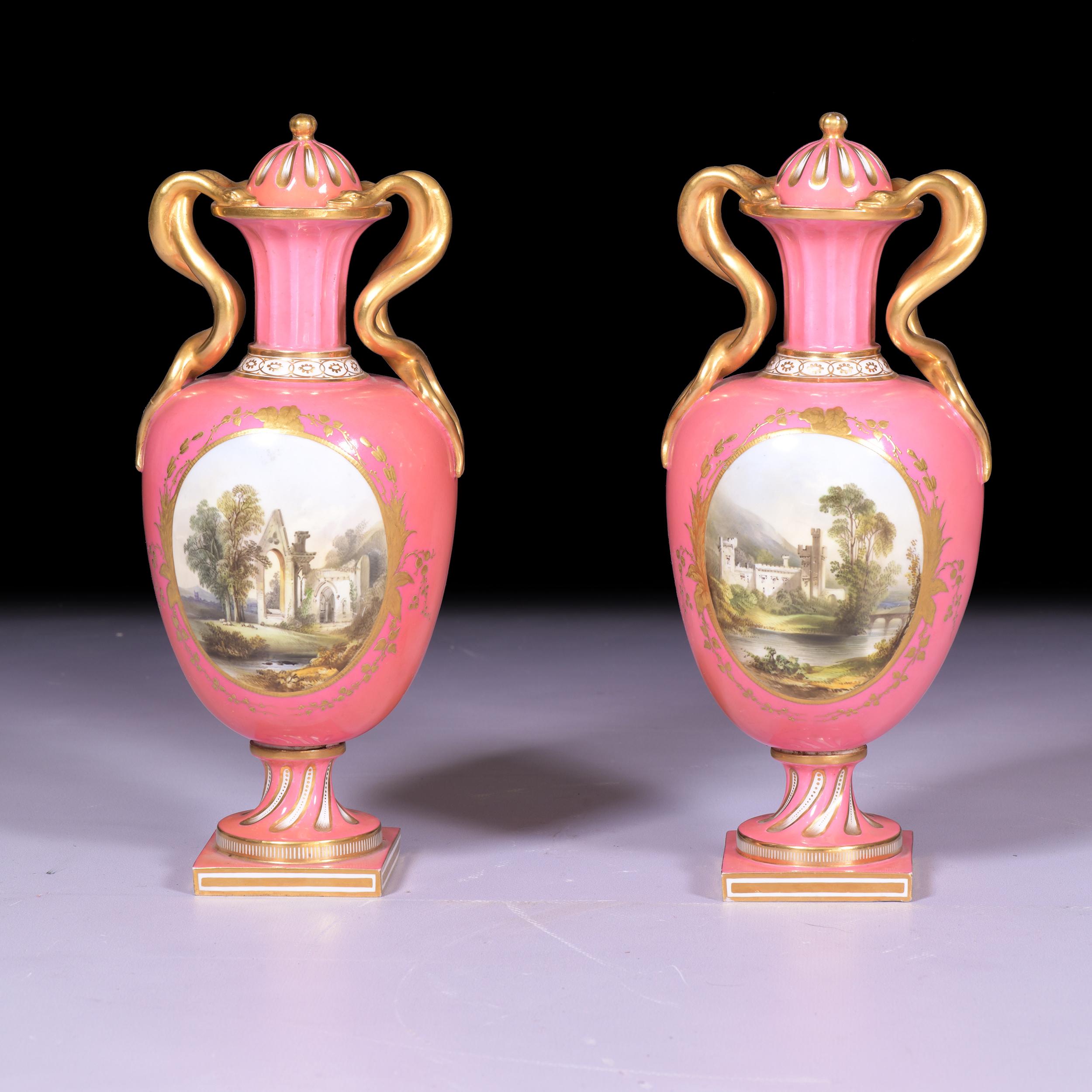 A pair of Coalport vases and covers, circa 1860, with ovoid bodies, gilded entwined serpent handles and fluted necks and feet, painted on both sides with oval landscapes of ruinous churches, a castle and a lakeland scene, reserved on bright pink