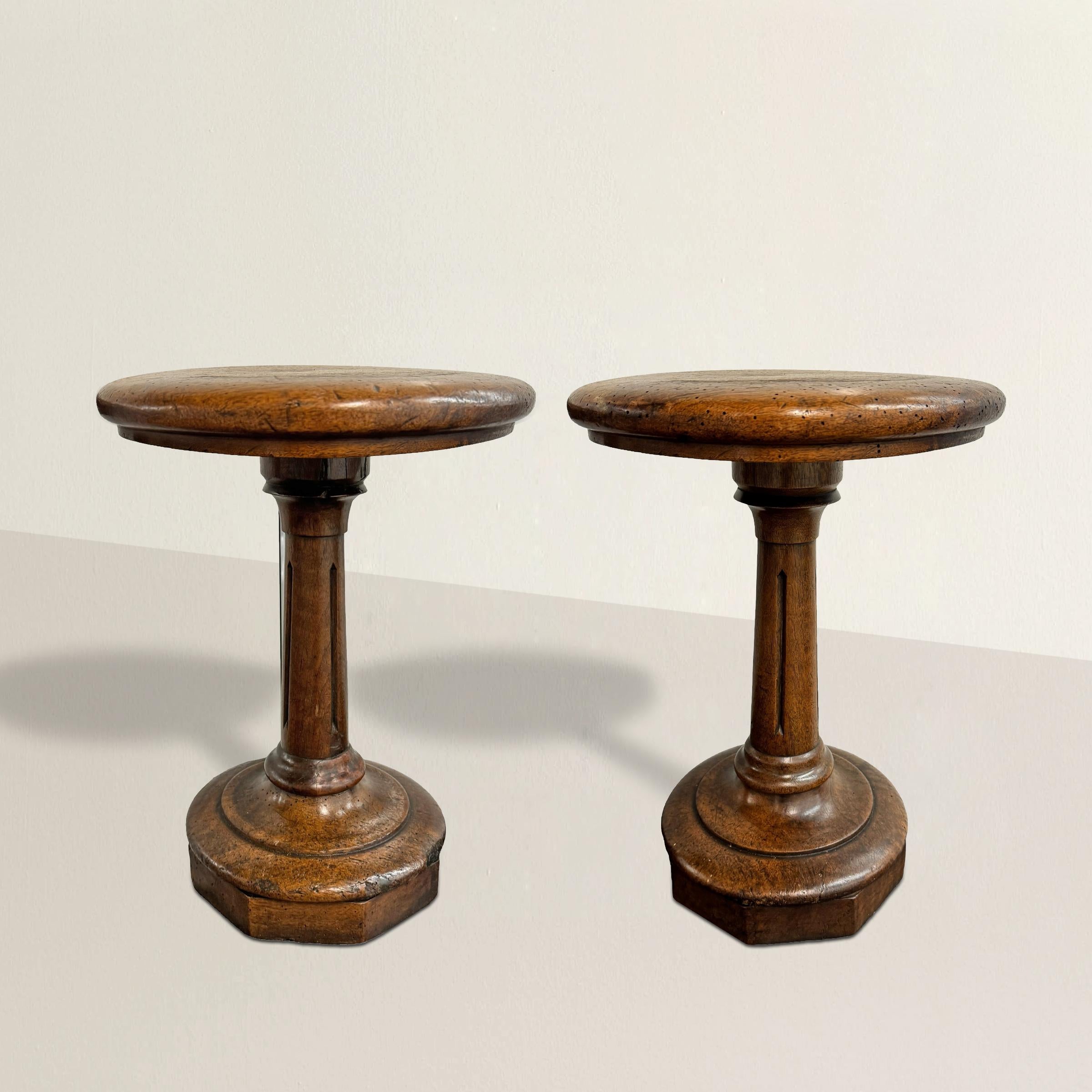 Crafted with care and boasting a rich history, these 19th century English pub stools feature well-worn round seats that whisper tales of convivial gatherings. They're supported by stylized fluted columns adorned with delicately carved arrow details,