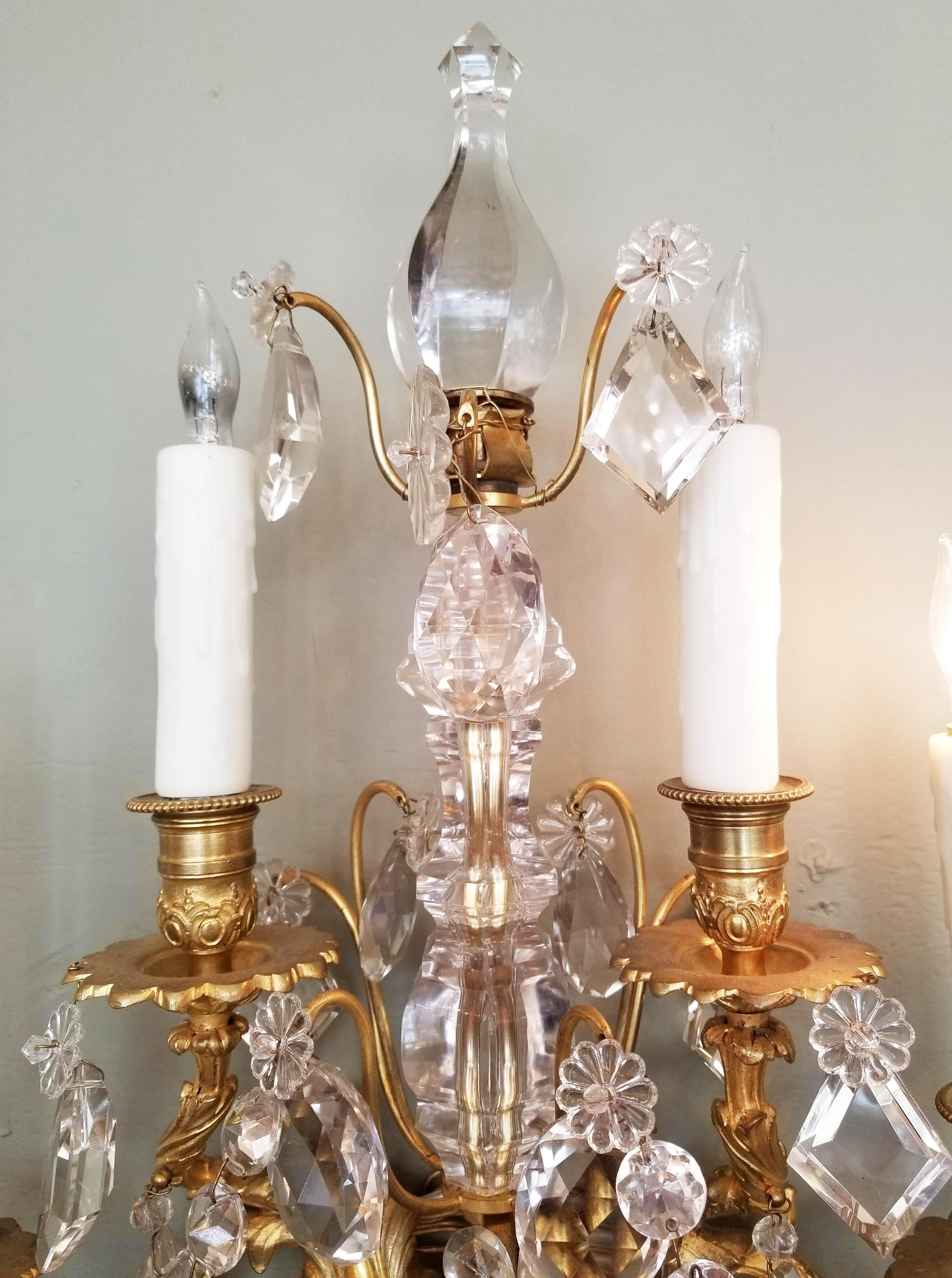 This elegant pair of Regency doré sconces, 19th Century, possibly 1820, feature a crystal top finial above four doré chased bronze candle arms that are accented with crystal swags and pendants. The center of the sconces have large Irish cut crystal