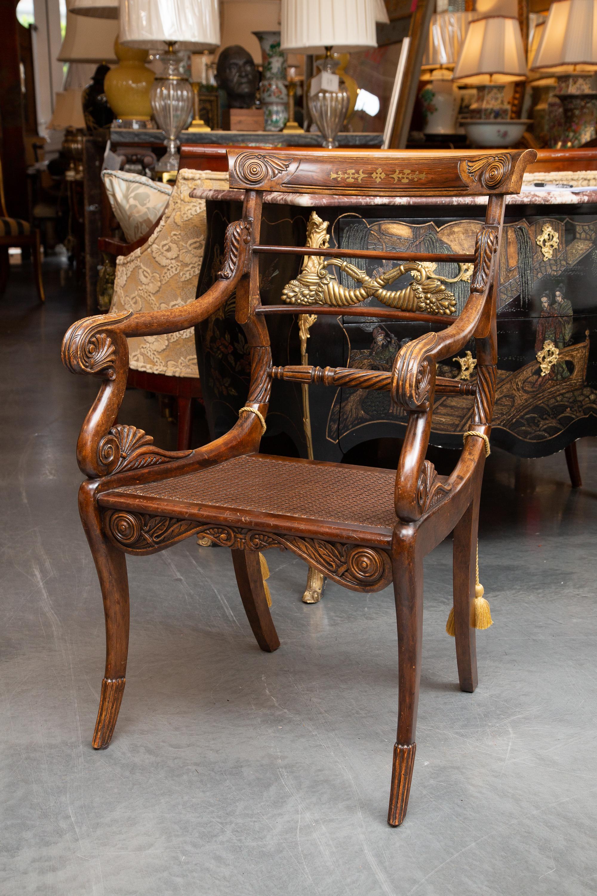 This is a stately pair of English mahogany Regency arm chairs, the top splat inlaid with brass. The smaller splats contain a pair of brass cornucopia over a caned seat and flanked by out-scrolling arms, supported by klismos legs, mid-19th century.