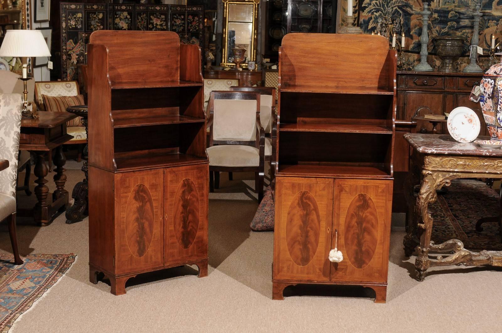A pair of 19th century English Regency style mahogany bookcases featuring inlaid lower cabinet doors ending on bracket feet.