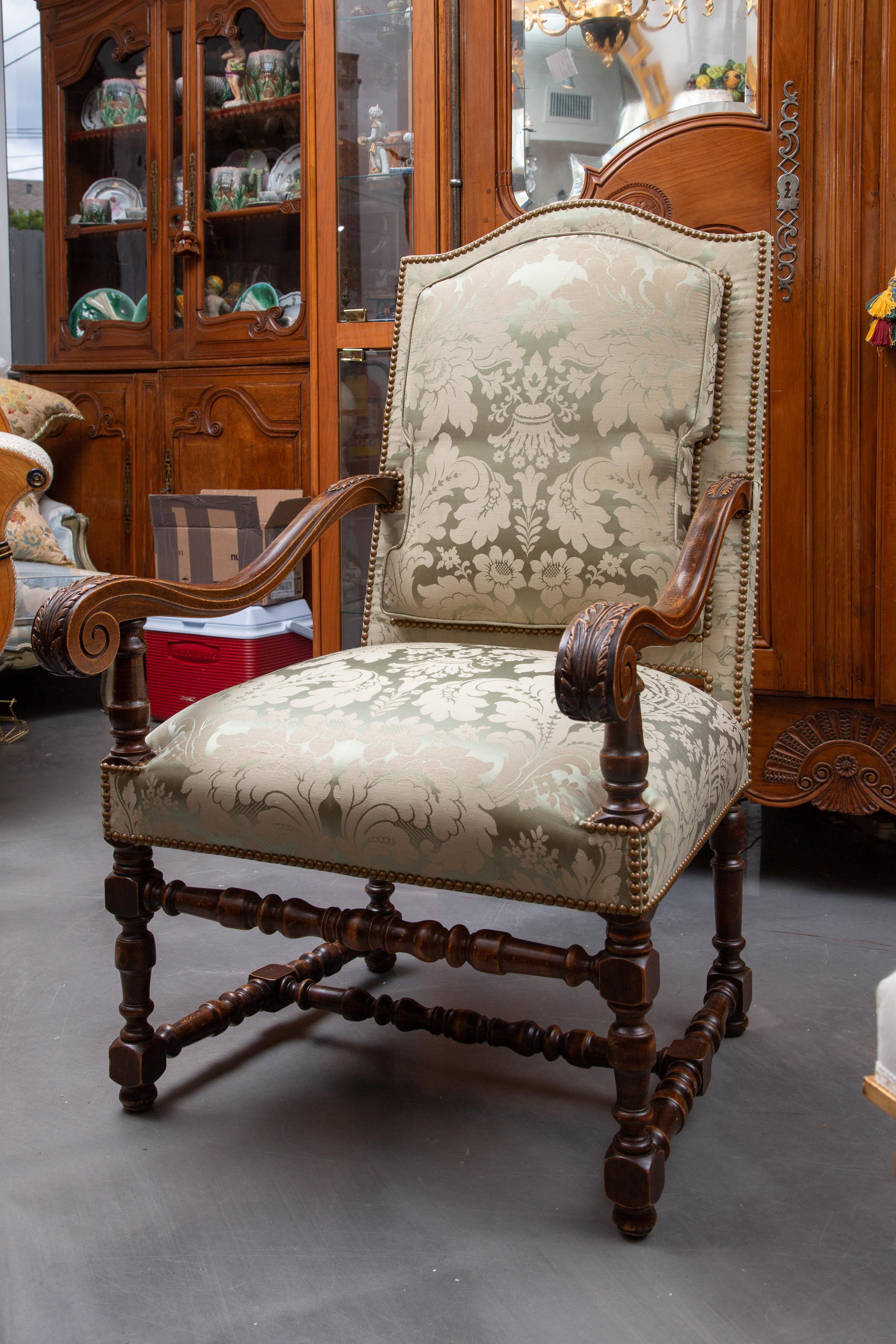 This is a stately pair of English walnut upholstered library chairs with fully padded back over fully padded seat, flanked by out-scrolling arms with acanthus carvings, and raised on baluster legs and cross-stretchers, late 19th century.