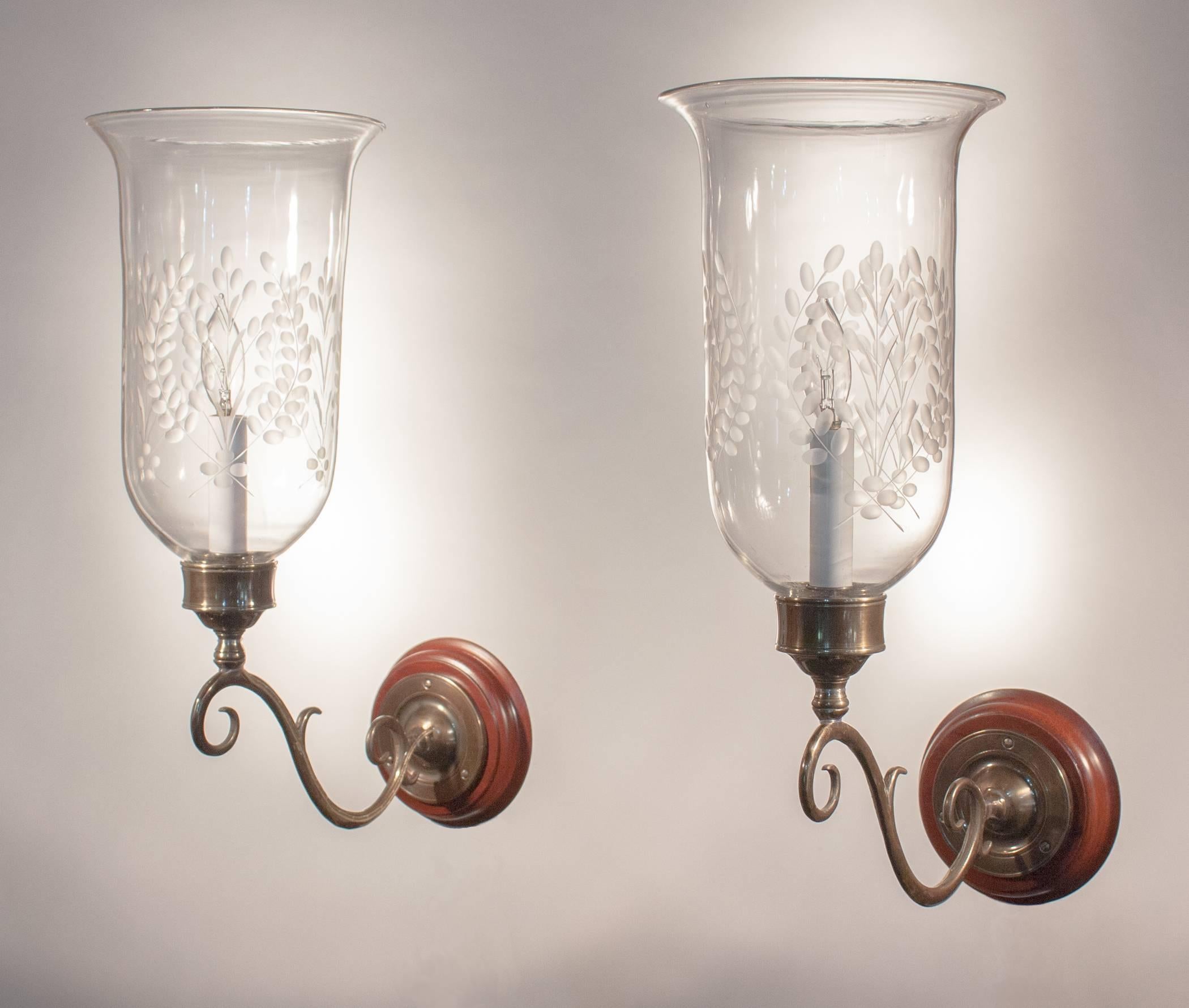 A pair of English hurricane sconce shades with a graceful flare and etched wheat motif, circa 1890. Small air bubbles in the handblown glass speak to both the quality and age of the shades. Custom-fabricated brass sconce arms and mahogany backplates