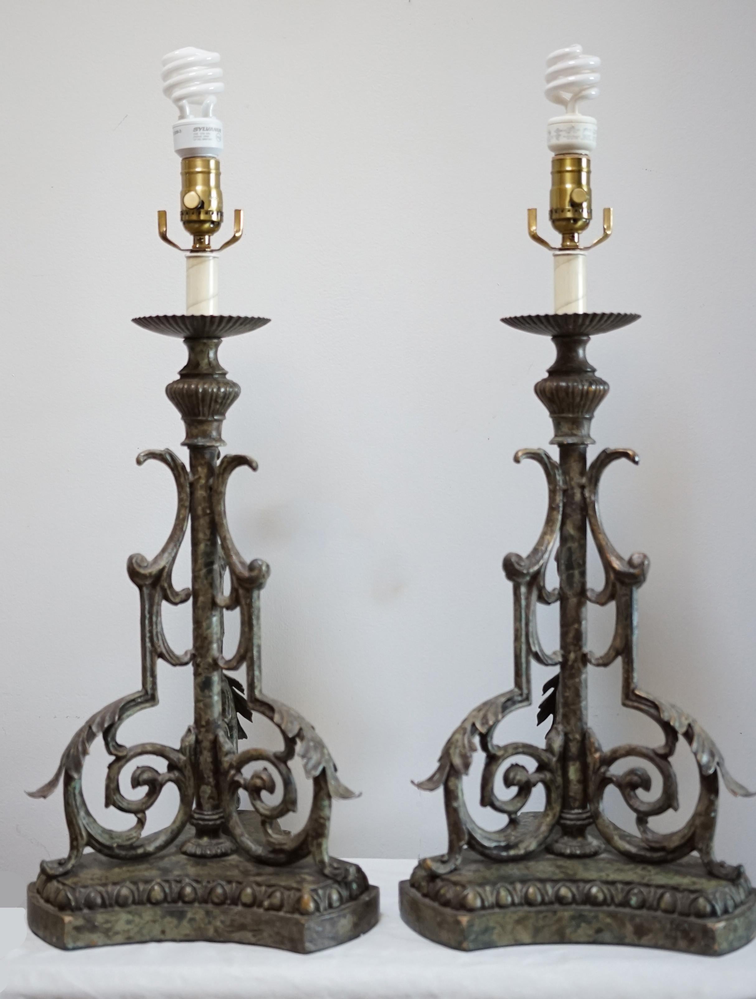 
This beautiful pair of hand wrought iron converted lamps once lit the way as pricket candleholders, and it surely took two hands to hold one. They are heavy, handcrafted beautifully, formed lamp conversions with a verdigris finish and a patina that