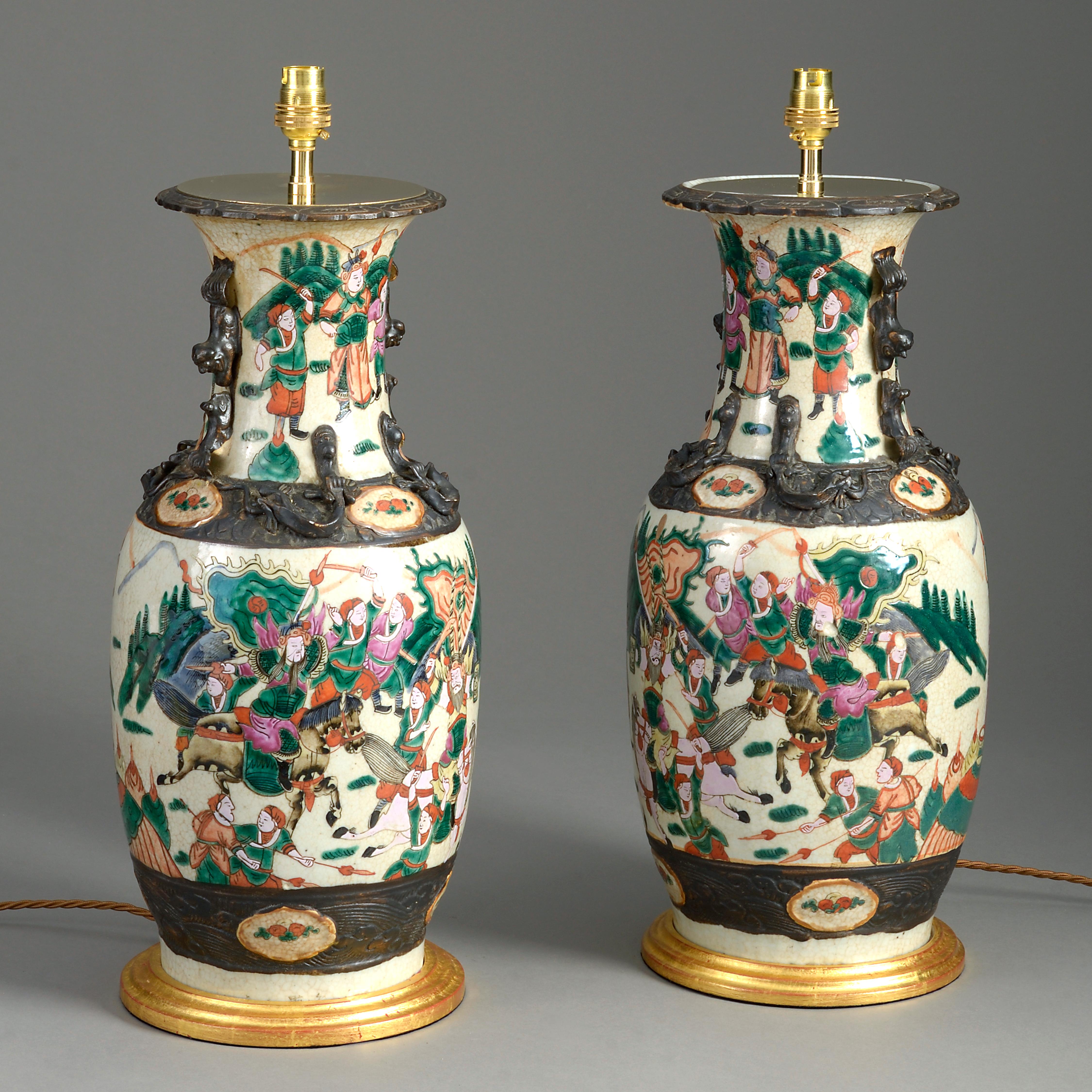 A late 19th century pair of famille verte porcelain vases, decorated throughout with figurative battle scenes. Now mounted on turned giltwood bases as lamps.

Height dimensions refer to combined height of vases and giltwood bases only.

Wired