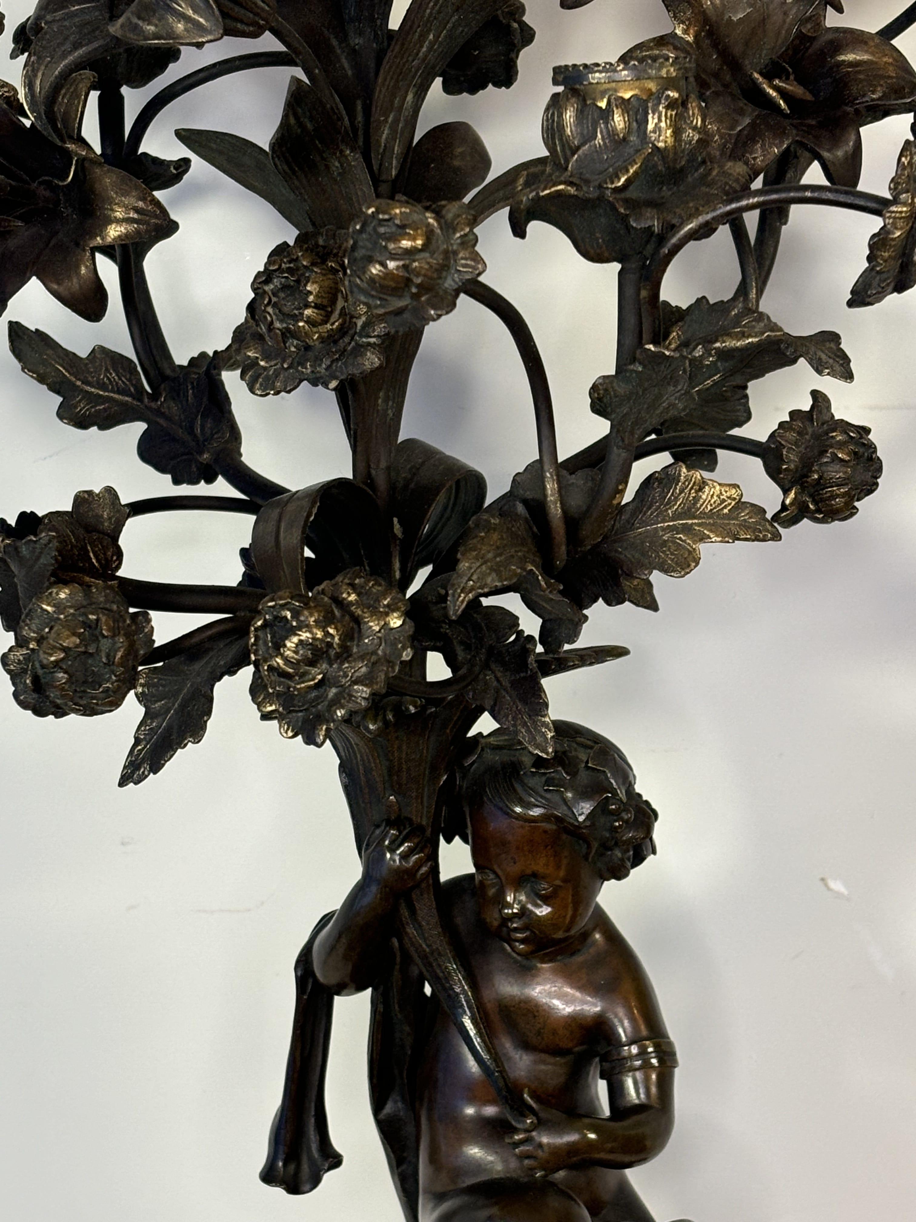 From Napoleon III period. Beautiful and rare pair of large bronze candelabras with brown patina, decorated with putti holding a cornucopia of abundance with a bouquet of five-light flowers, with two extinguishers at the top. Black marble bases. 