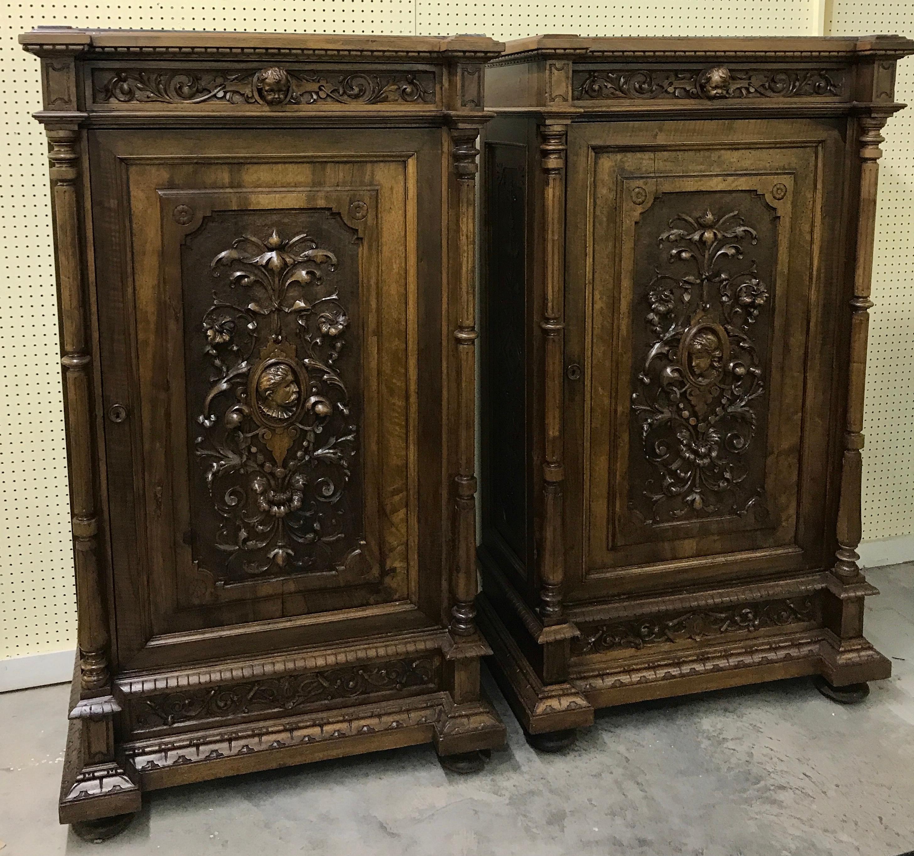 A pair of Flemish carved walnut and marble cabinets, each one with removable canted inset gray marble tops, with one angel head frieze drawer, over the Florentine carved case, fitted with one door.
One cabinet is carved with a male medallion head