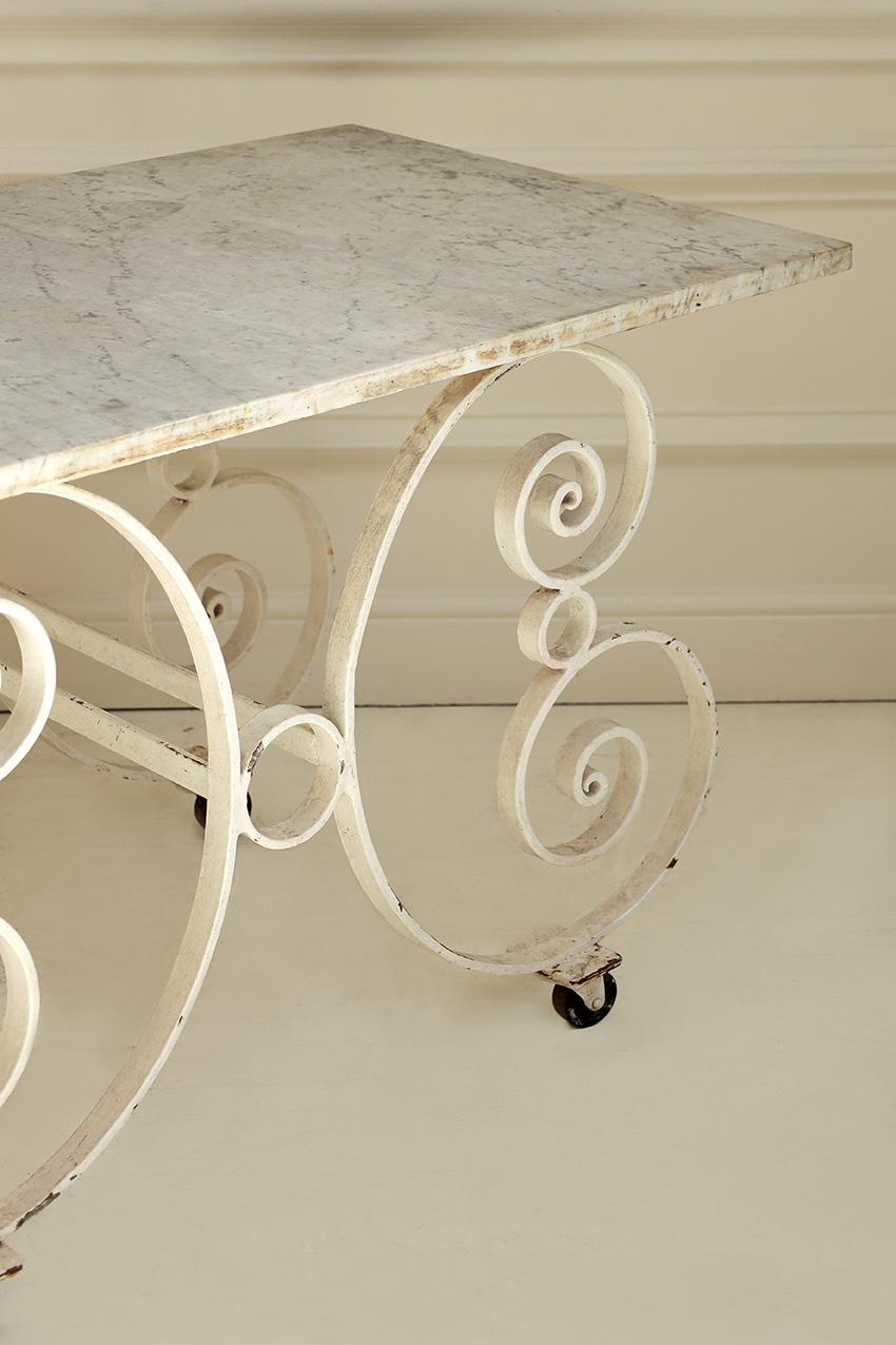 Un par de mesas de panadero francesas bellamente envejecidas, que combinan una forma elegante con una función práctica. Cada mesa tiene una elegante base de hierro forjado a mano con volutas decorativas, acabada en una suave pátina blanca desgastada
