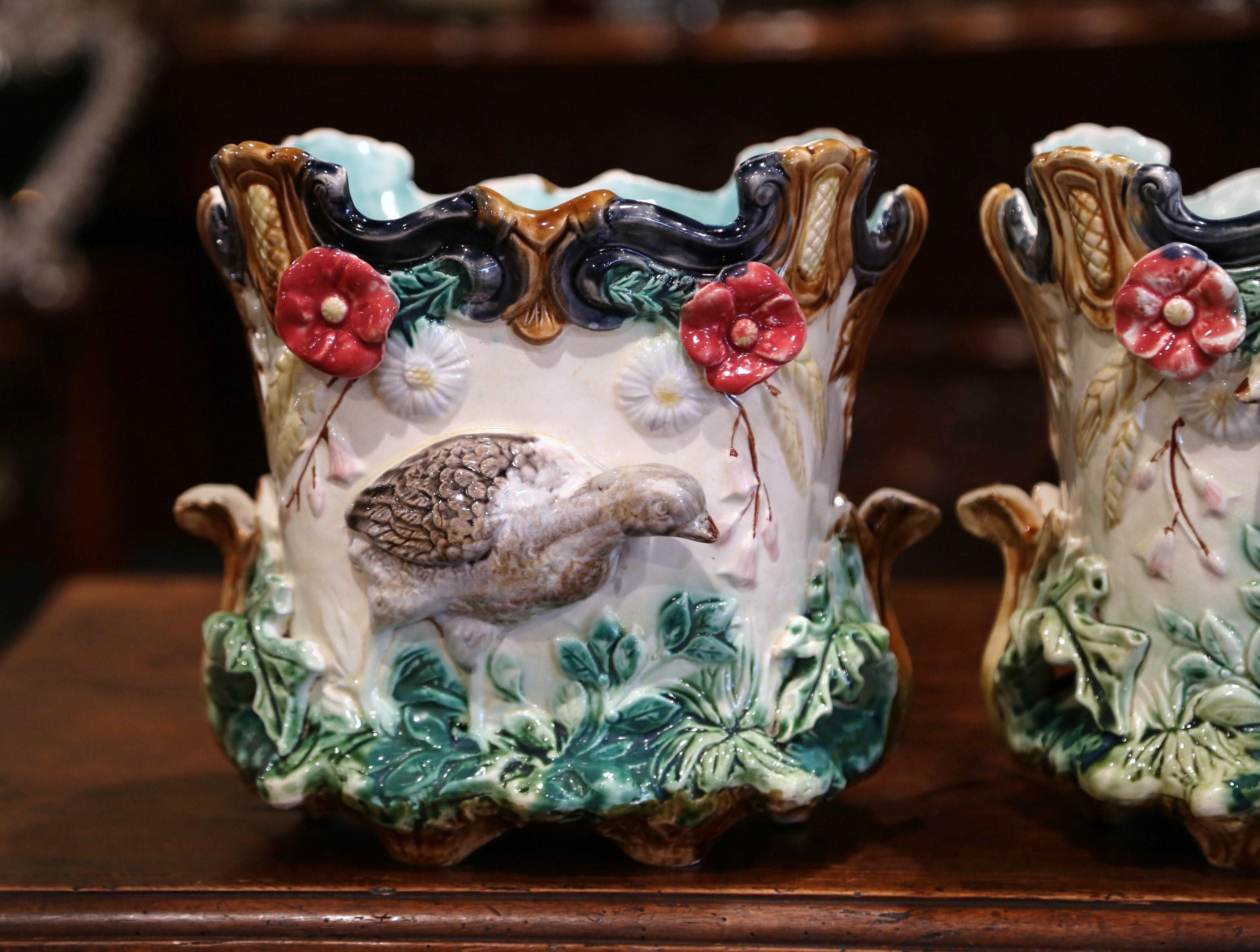 This pair of colorful, hand painted Majolica jardinières was sculpted in France, circa 1870. The antique planters are almost square in shape with scalloped decor around the edges. Each porcelain cachepot features exquisitely rendered hunt and floral