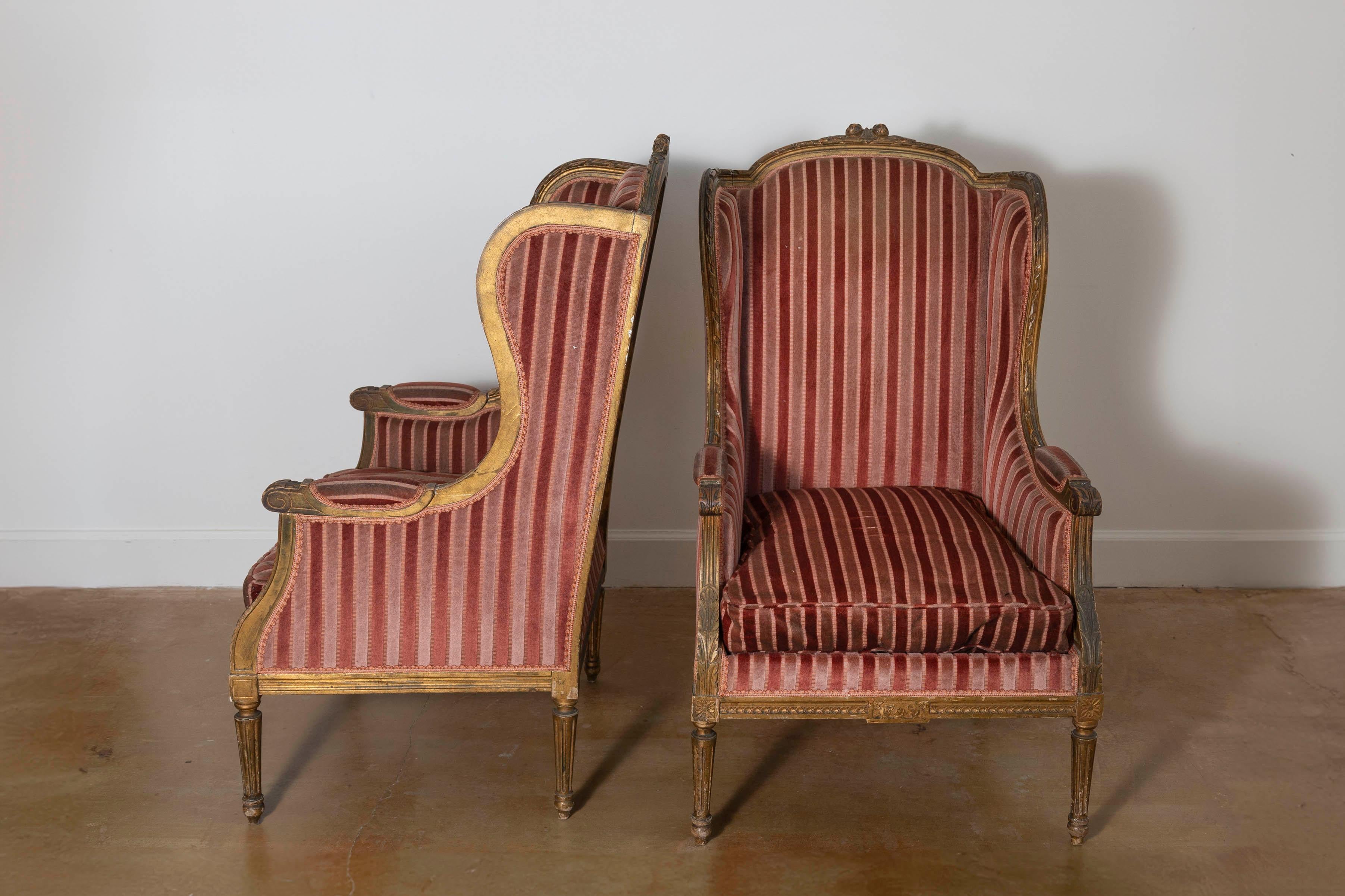 Questa coppia di bergères francesi del XIX secolo emana un'eleganza senza tempo e incarna la raffinata maestria dello stile Luigi XVI. Le cornici in legno intagliato, probabilmente realizzate in legno dorato, presentano dettagli intricati, tra cui