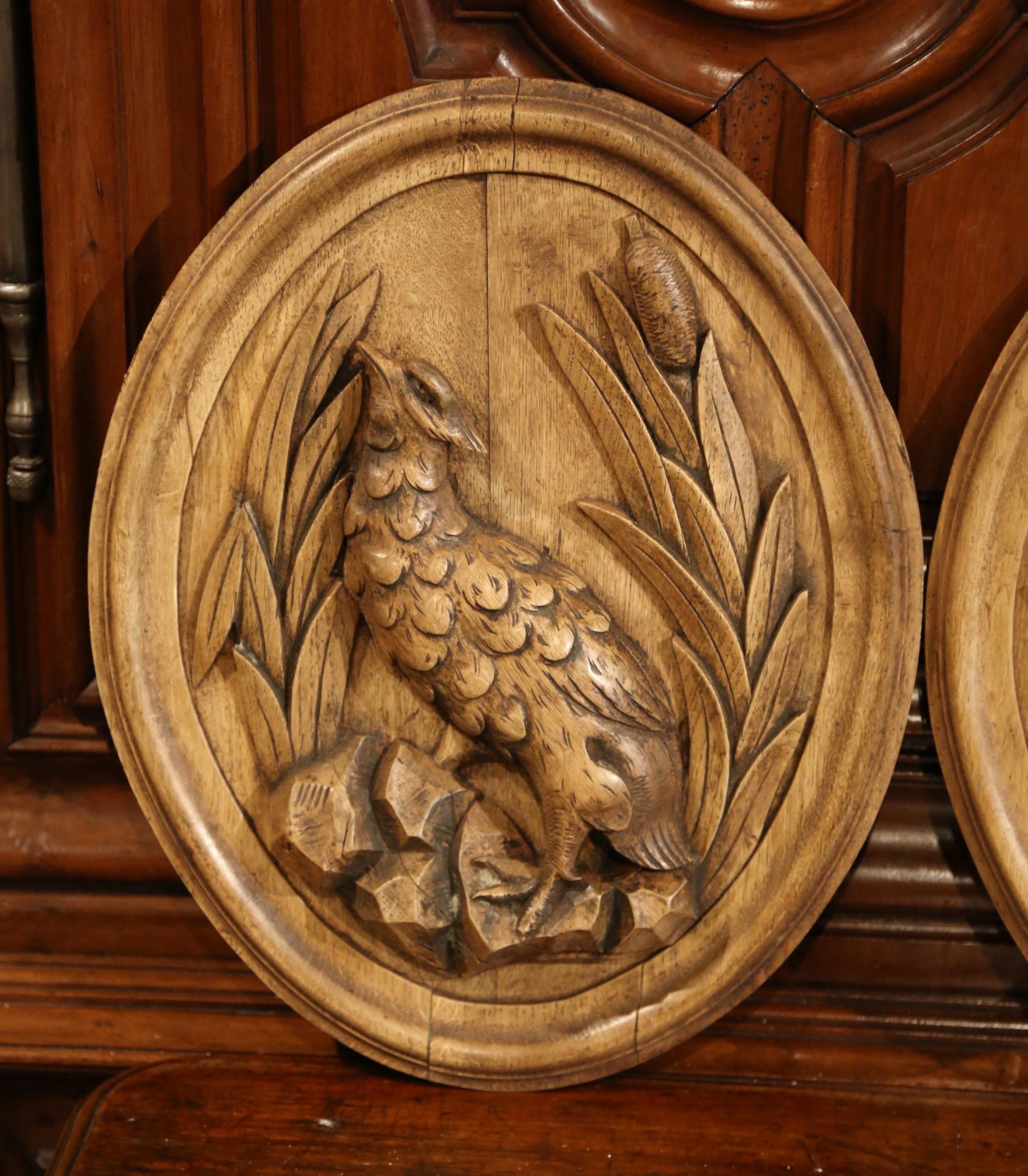 This pair of antique Black Forest bird sculptures was crafted in France, circa 1870. Made out of oak, each oval wooden plaque features a hand carved partridge in high relief standing on rocks with tall reeds around. Both pieces have been stripped