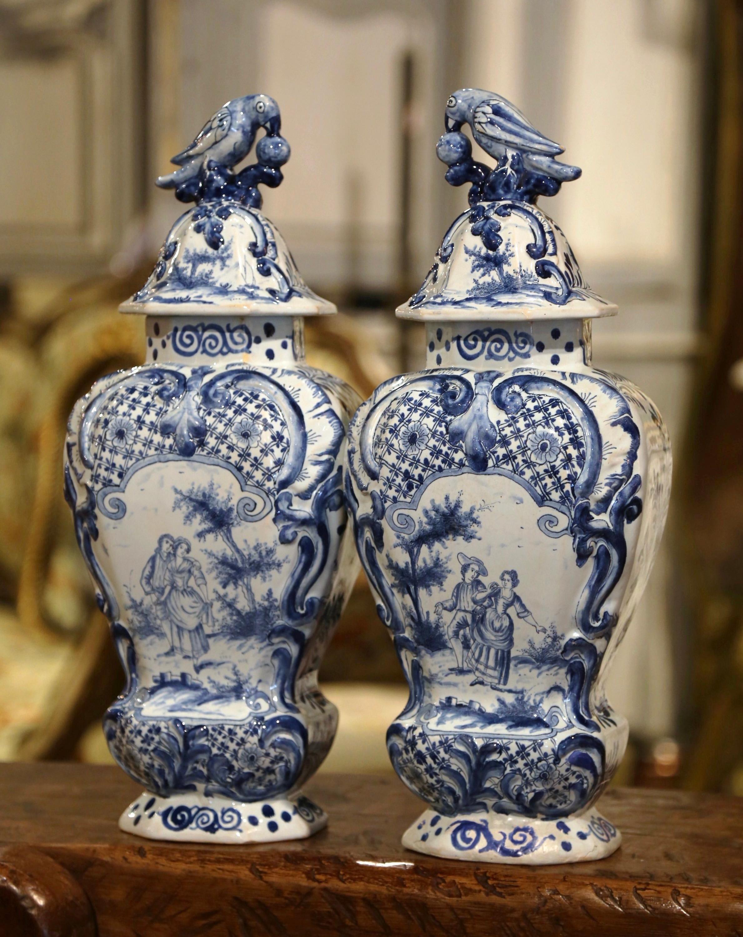 Ces vases classiques anciens de Delft ont été créés en France, vers 1860. Chaque pot élégant en porcelaine est décoré de médaillons de scènes romantiques finement peints et agrémenté d'un décor floral en haut-relief. Chaque couvercle est orné d'une