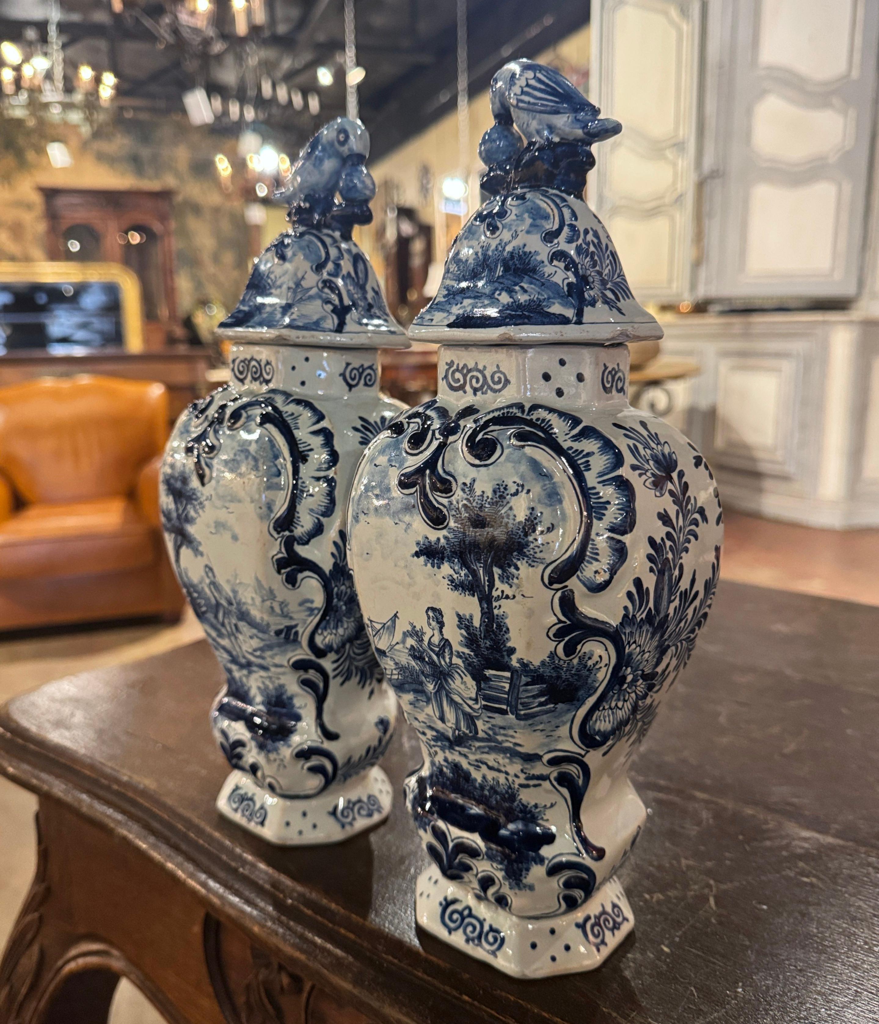 Ces vases Delft classiques ont été créés en France vers 1860. Chaque élégante jarre en porcelaine est décorée de médaillons de scènes romantiques finement peints et rehaussés d'un décor floral en haut-relief. Chaque couvercle est orné d'un oiseau