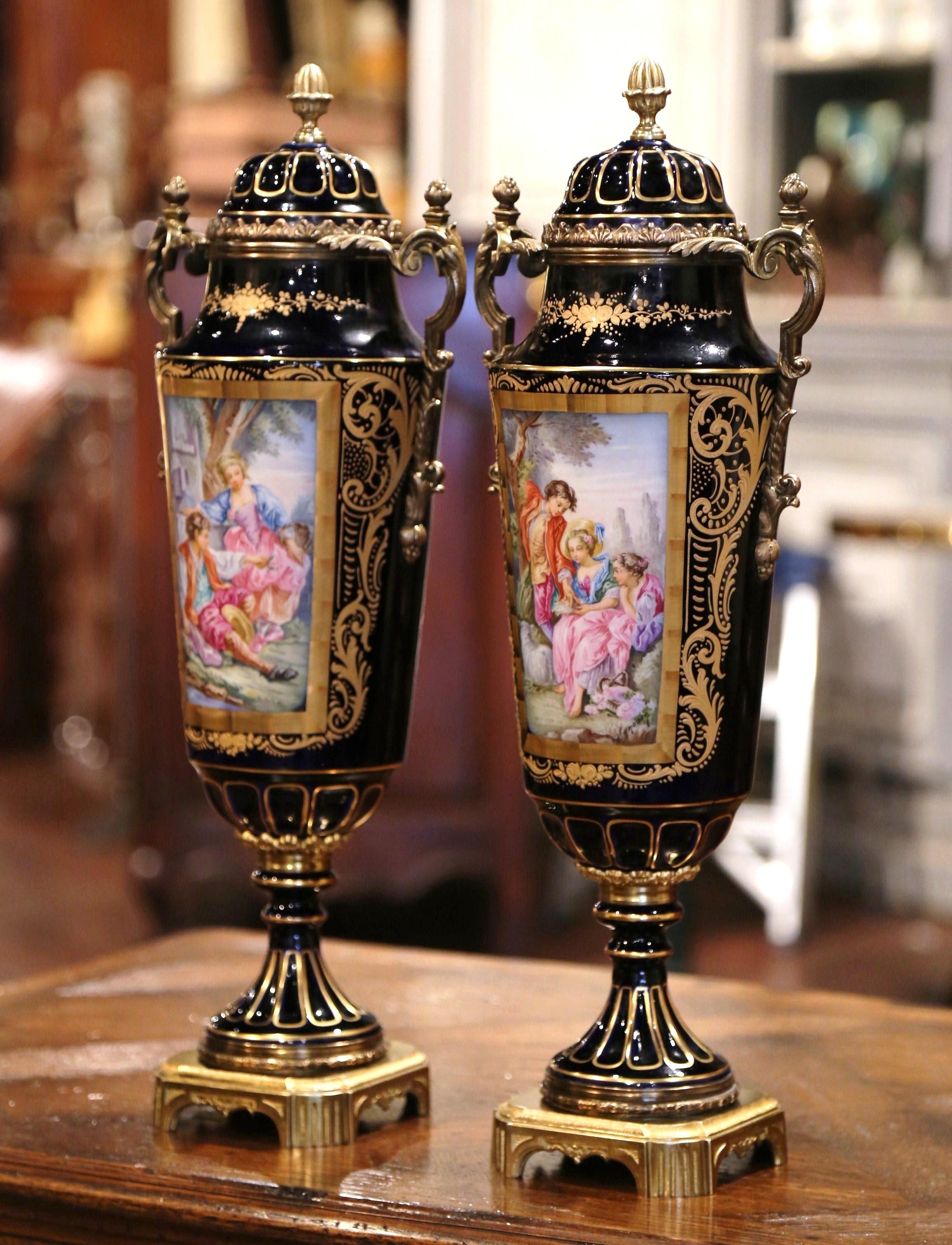 Decorate a mantel or a console with this elegant pair of porcelain and bronze urns. Created near Paris, France, circa 1880, each impressive, decorative vase sits on a square bronze base, and has a cone shaped finial on the lid. The urns are