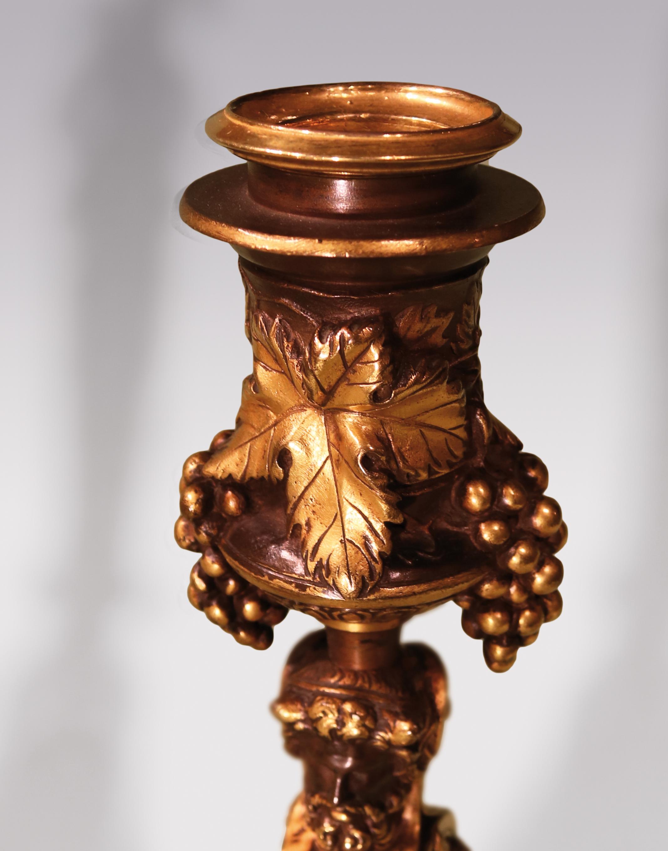 An unusual pair of mid-19th century French bronze and ormolu candlesticks, having grape and vine nozzles raised on swaged, fluted tapering stems surmounted by classical busts of man and woman, ending on decorated and beaded circular bases. Signed F.