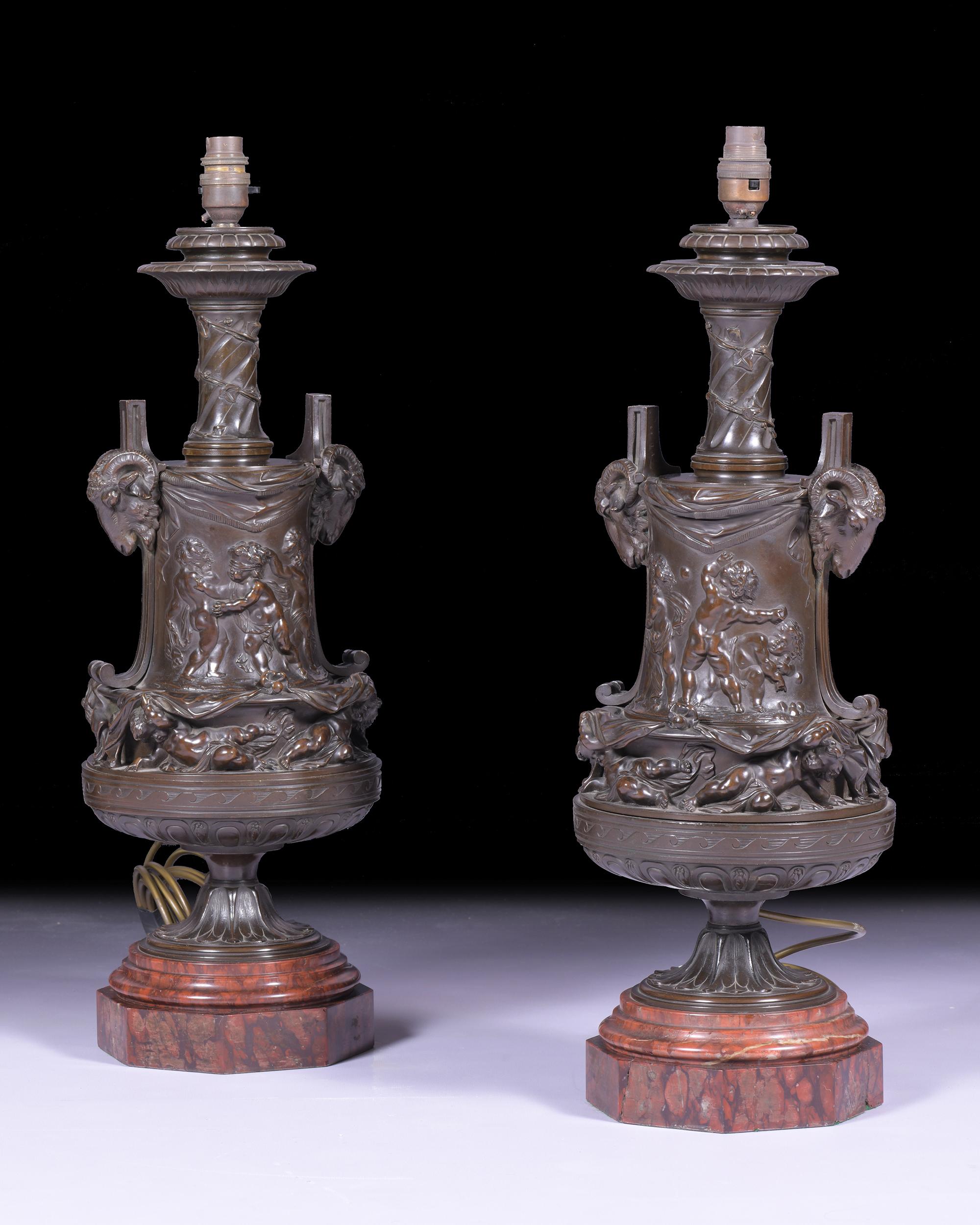 Une superbe paire de lampes en bronze du XIXe siècle, avec des scènes classiques représentant des chérubins gambadant en relief, flanqués de masques à tête de chèvre sur les côtés, sur des bases en marbre rouge à gradins se terminant sur une base de