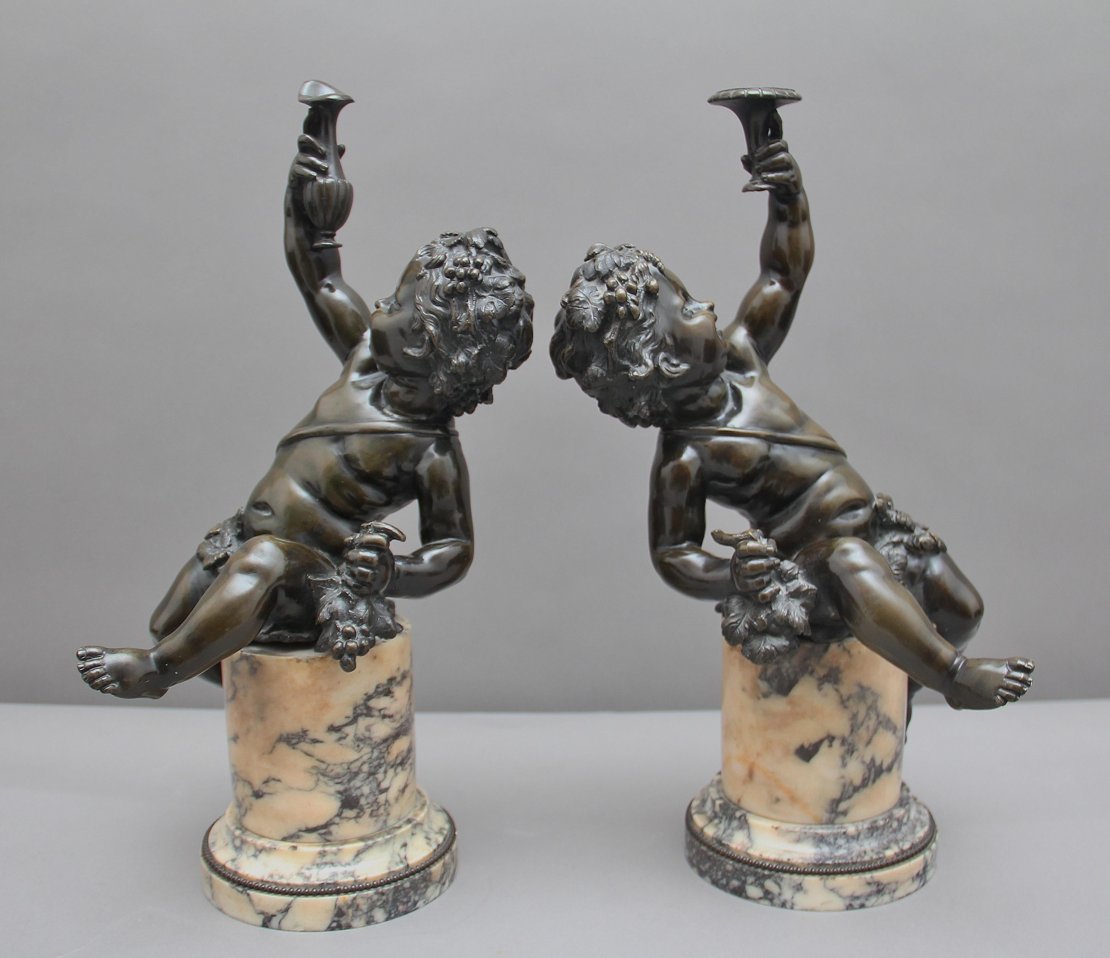 A superb pair of 19th century French putti on marble bases, the young Bacchanalian putti seated unsteadily on integral cylindrical variegated marble beaded and stepped pedestal bases, holding aloft a ewer, tazza and bunch of grapes. These pair of