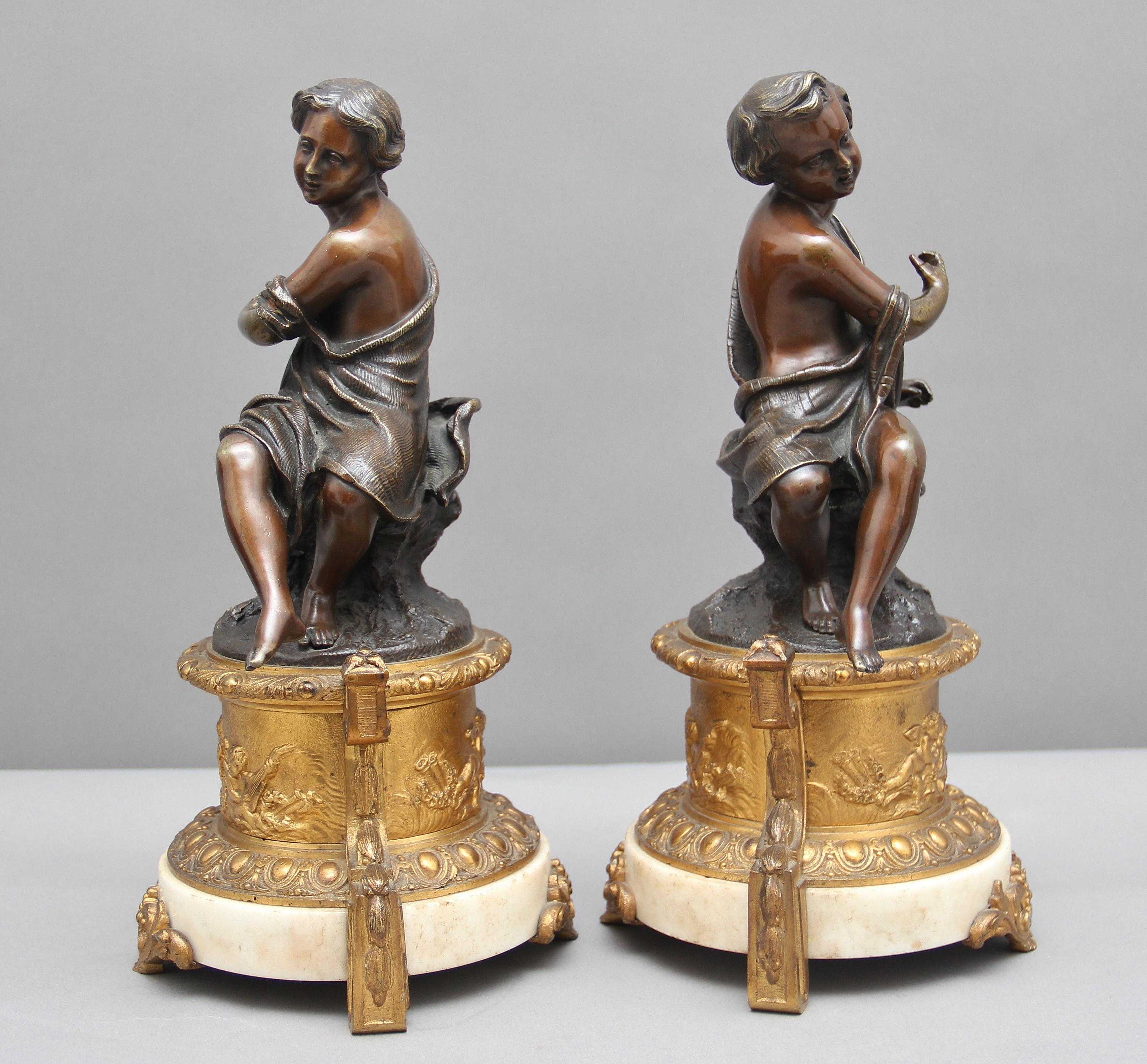 A pair of 19th century French bronze figures of a boy and girl, each figure seated and dressed in robes, supported on finely cast gilt bronze cylindrical plinths which is cast with opposing musical putti, within classical form uprights to further