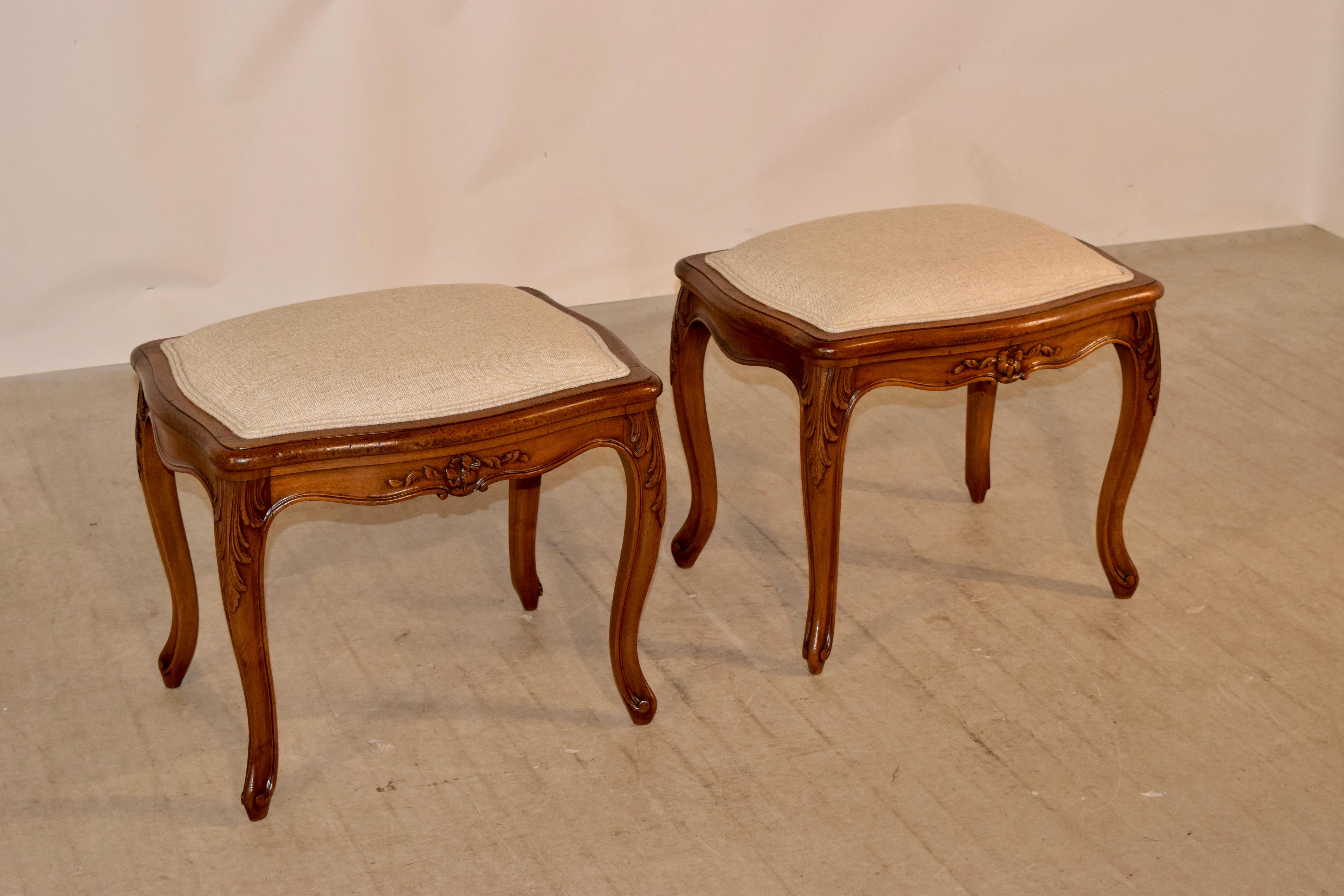 Pair of 19th century walnut stools from France with newly upholstered tops in linen, which are framed by scalloped and beveled edges around the border of the frame and following down to scalloped and hand carved decorated aprons and supported on