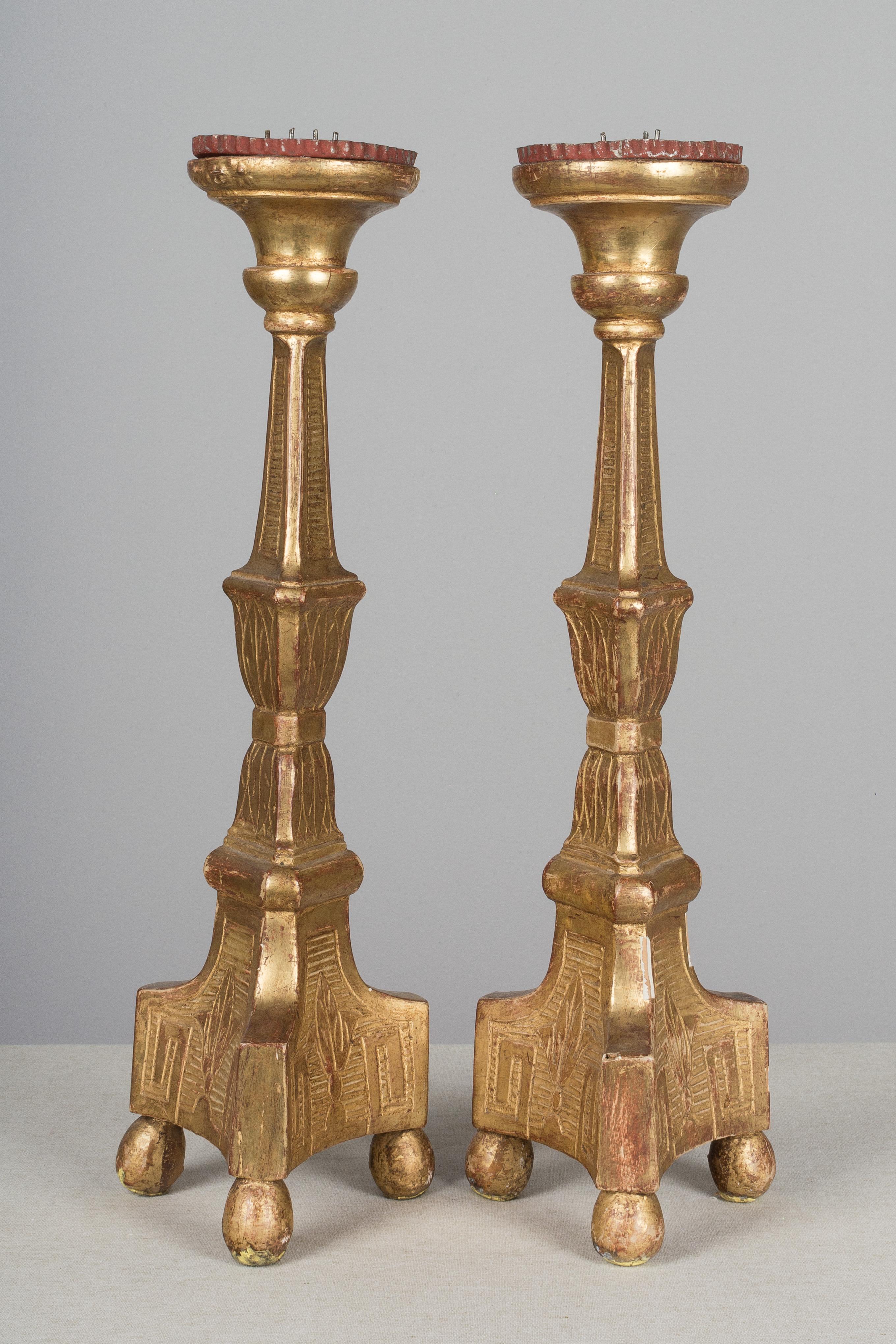 A pair of 19th century French giltwood altar candlesticks. Tall columns on a trefoil base. Zinc prickets. Original bright gilt finish. Gilt losses to both, one more than the other.