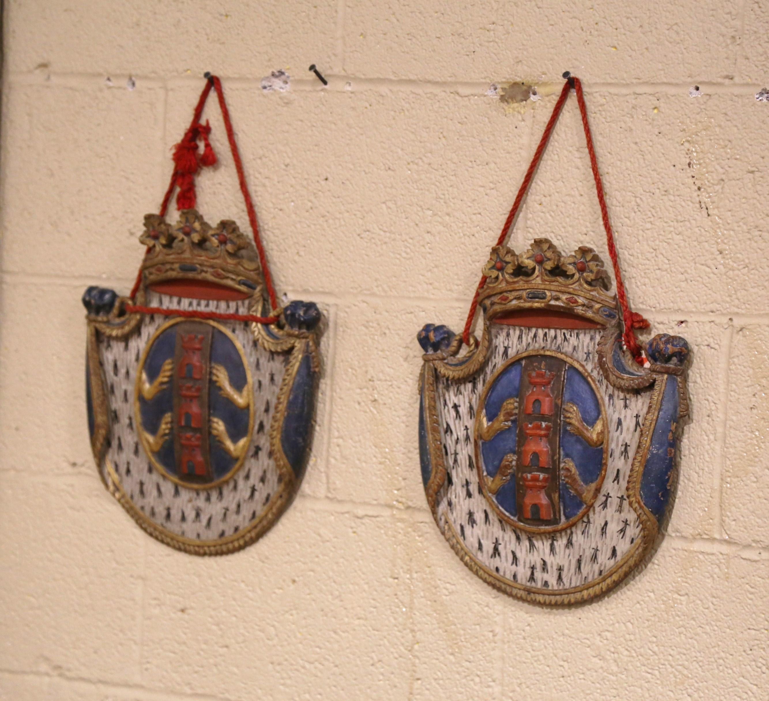 Embellish your study or library with this elegant and colorful pair of wall hanging coat of arms shields. Carved in France, circa 1880, each heraldic plaque features a top crown and carved folded sides topped with a floral finial. The center depicts