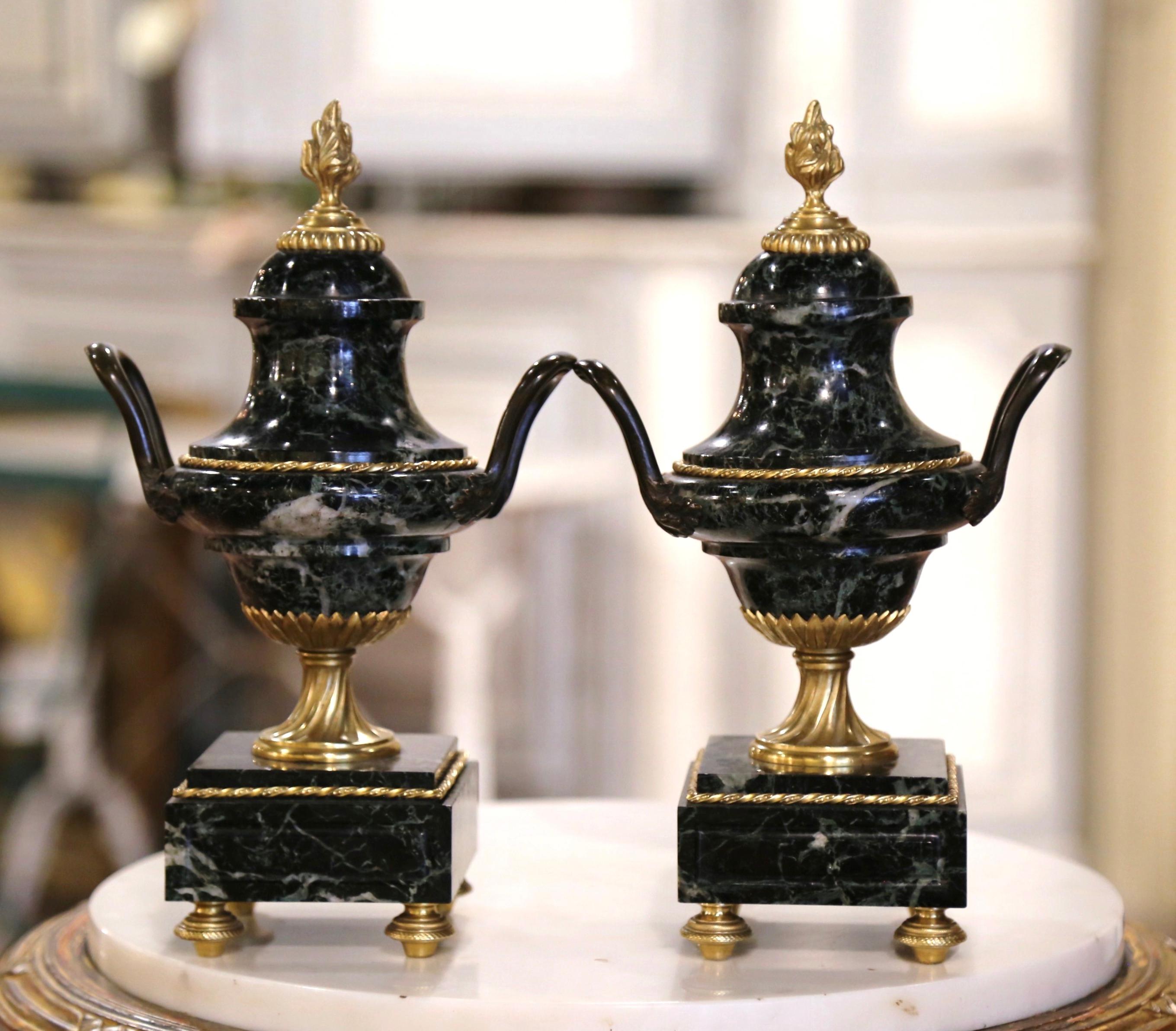 Crafted in France, circa 1890, these antique urns are carved of marble and stand on square bases ending with bronze rounded feet. Each vessel with bronze ring motif around, is dressed with a dome shaped lid embellished with a bronze flame form