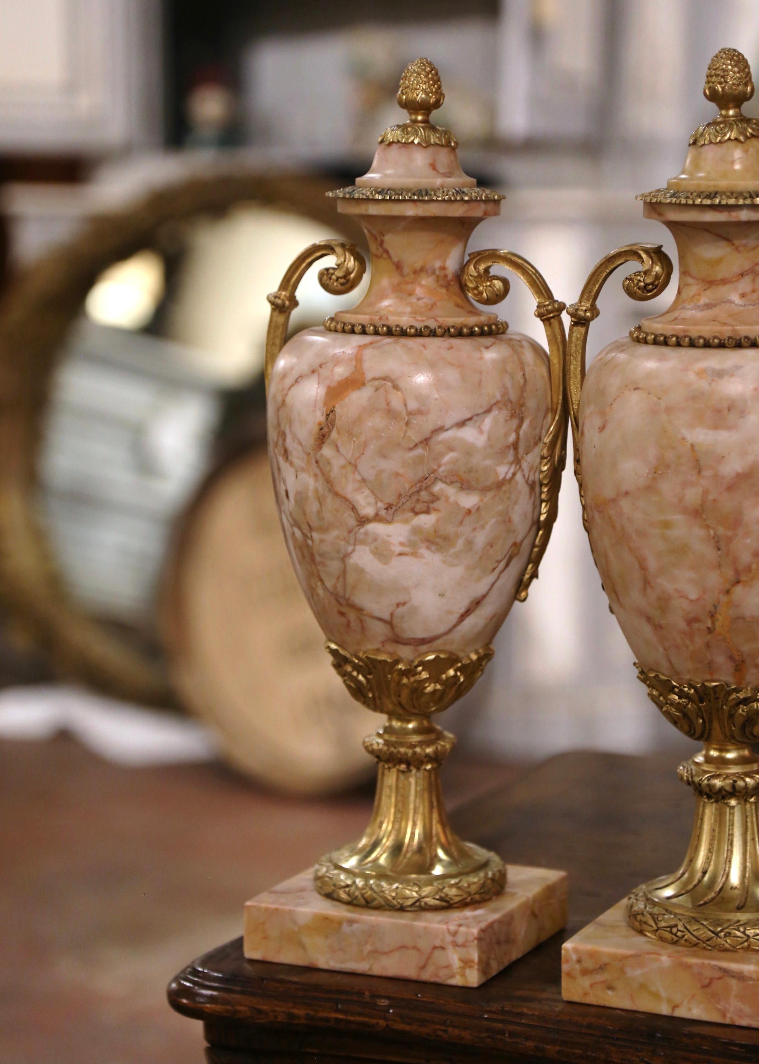 Decorate a mantel or a console with this elegant pair of antique Louis XVI cassolettes. Crafted in France, circa 1870, each urn made of marble stand on a square base decorated with acanthus and laurel leaf motifs. The marble vessel with ornate side