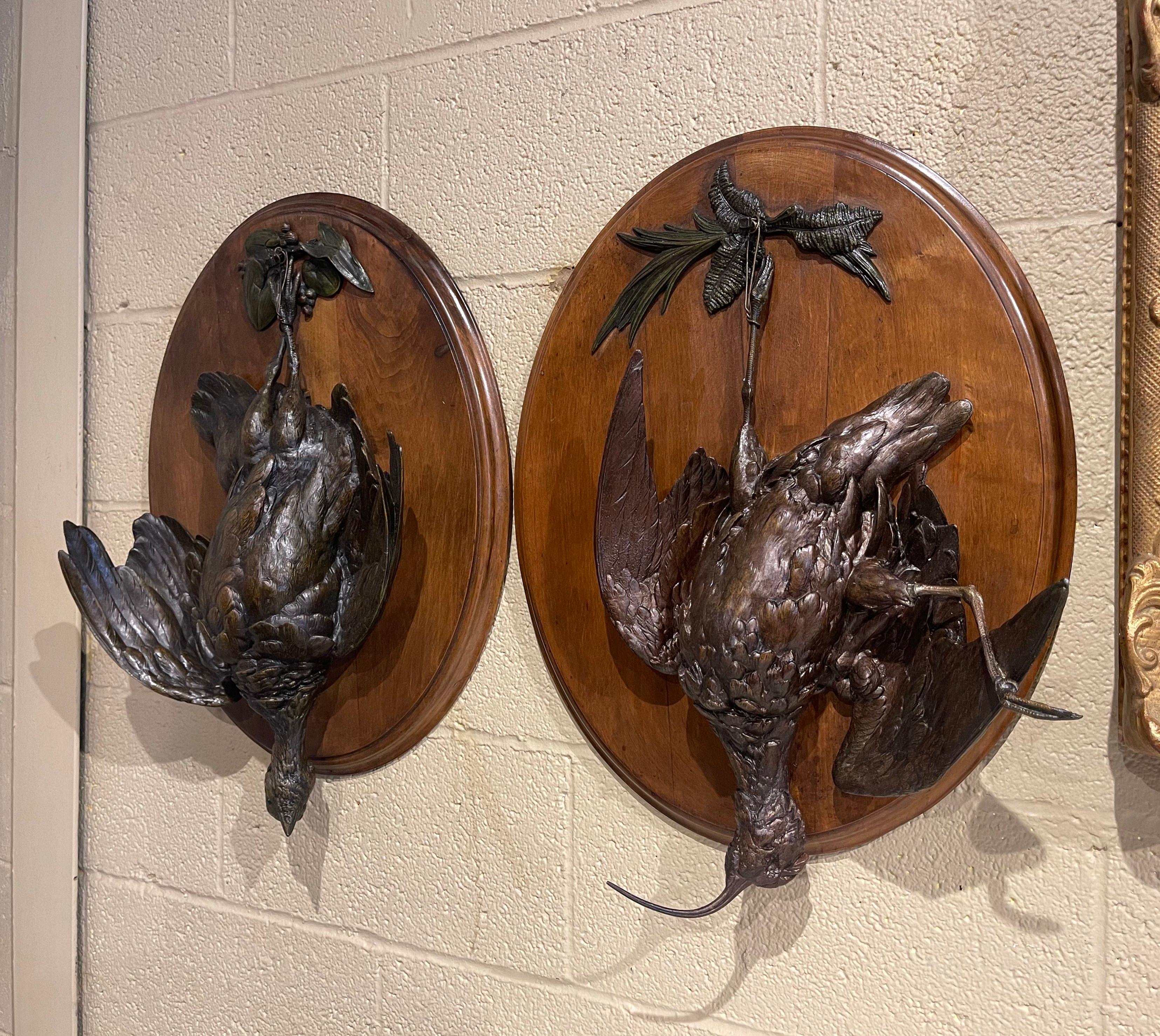 These large antique trophy plaques were created in France, circa 1880. Set on carved oval walnut boards, each wall hanging decor feature a detailed carved bird in high relief, tied upside down to foliage embellishments with a rope at the base. The