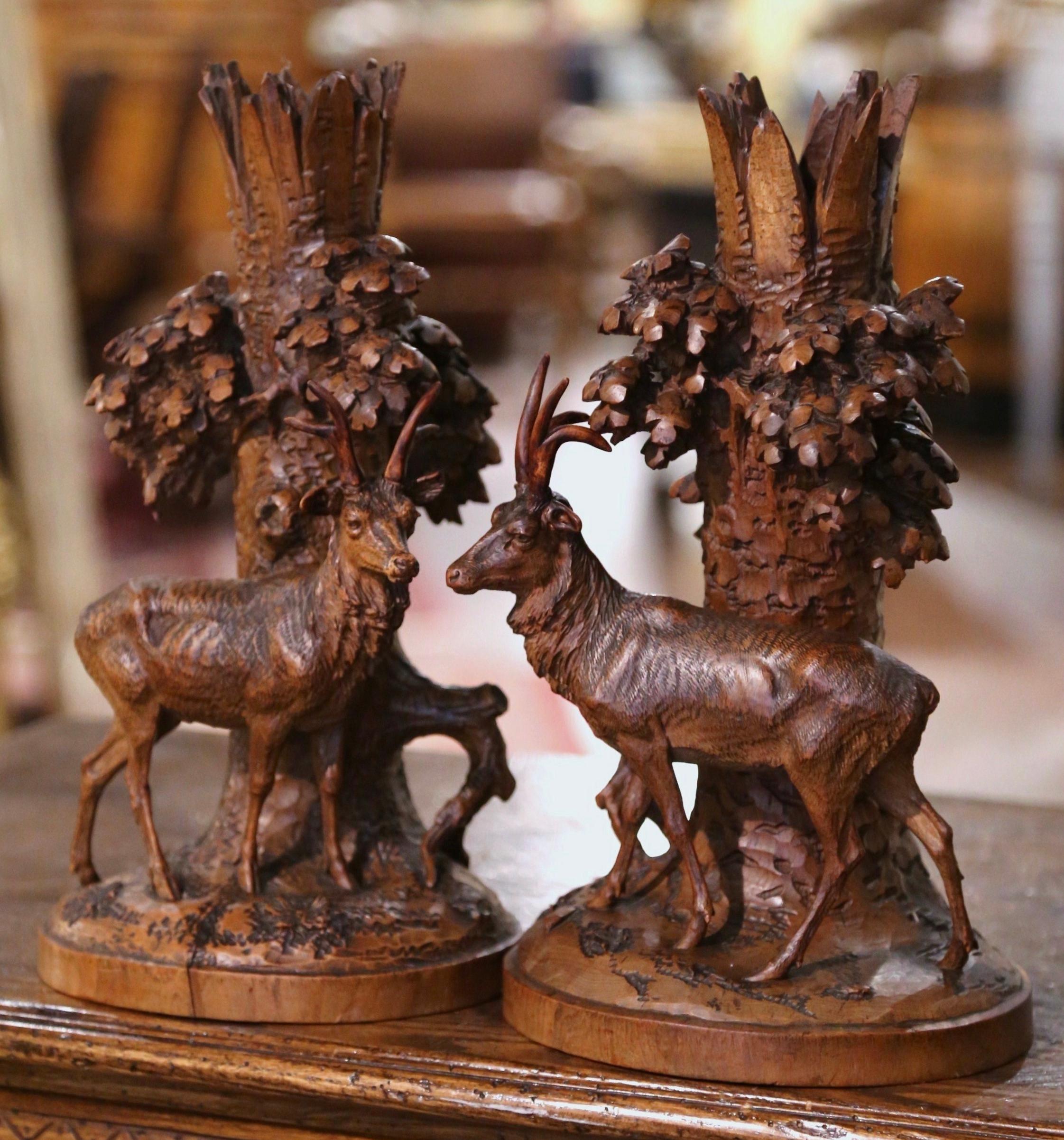 Decorate a mantel or a console table with this exquisite pair of Black Forest deer carvings. Created in France, circa 1860, and hand carved of walnut, each work composition depicts a buck standing in front of a tree trunk with hanging leaves coming