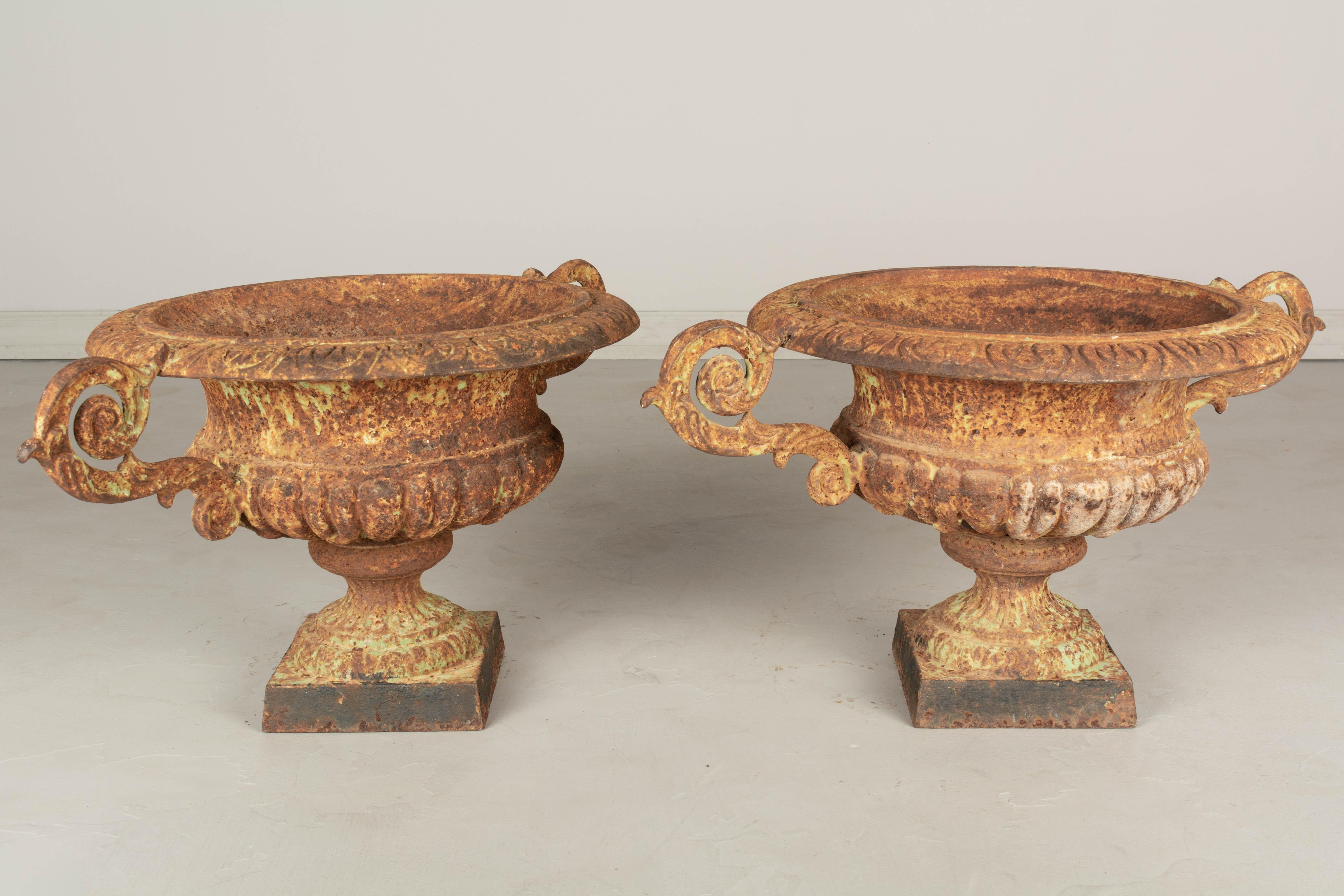 A pair of 19th century French cast iron garden urn planters, with weathered rusted patina and remnants of light green paint. Nicely cast details, especially on the double handles. 
14