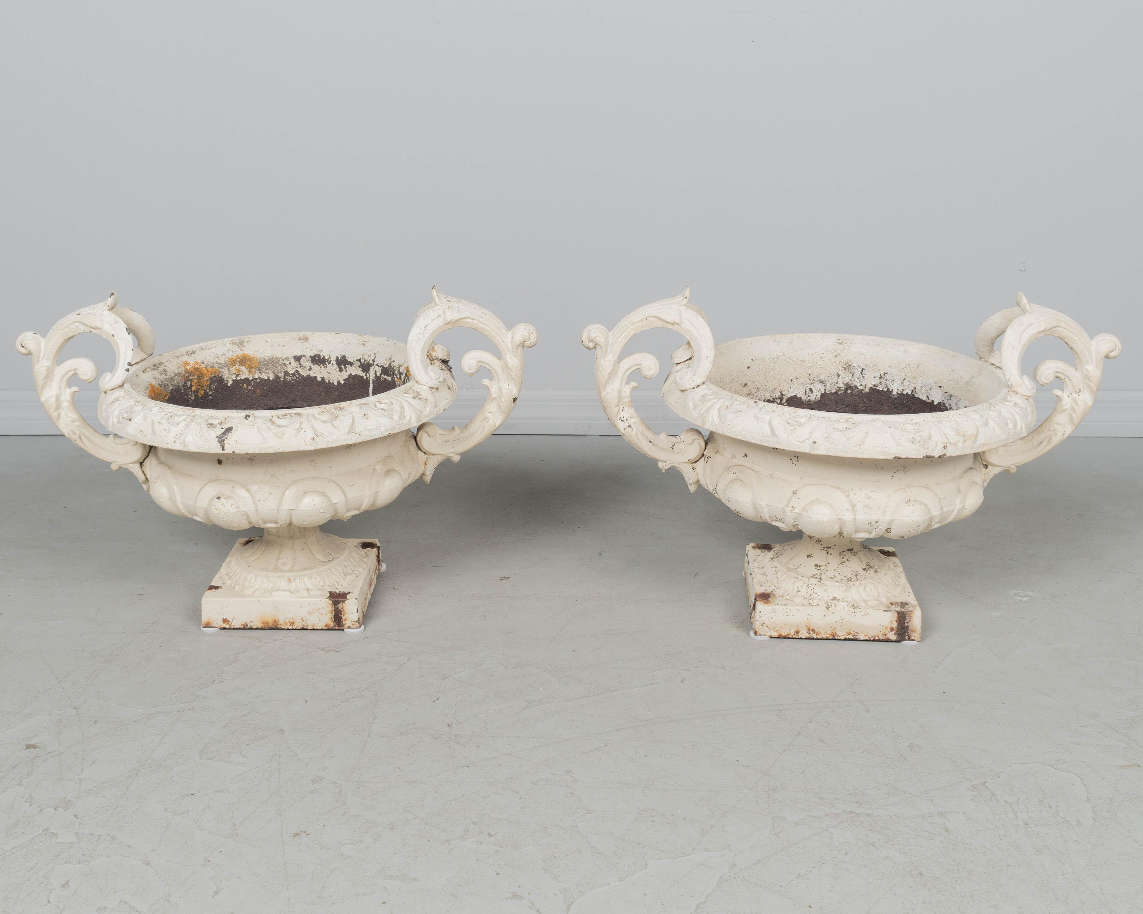 Paire de jardinières en fonte française du 19e siècle, avec base à piédestal et poignées à volutes. Patine de peinture blanche altérée par les intempéries avec quelques traces de rouille. Vers 1870-1890.
Dimension : 26 