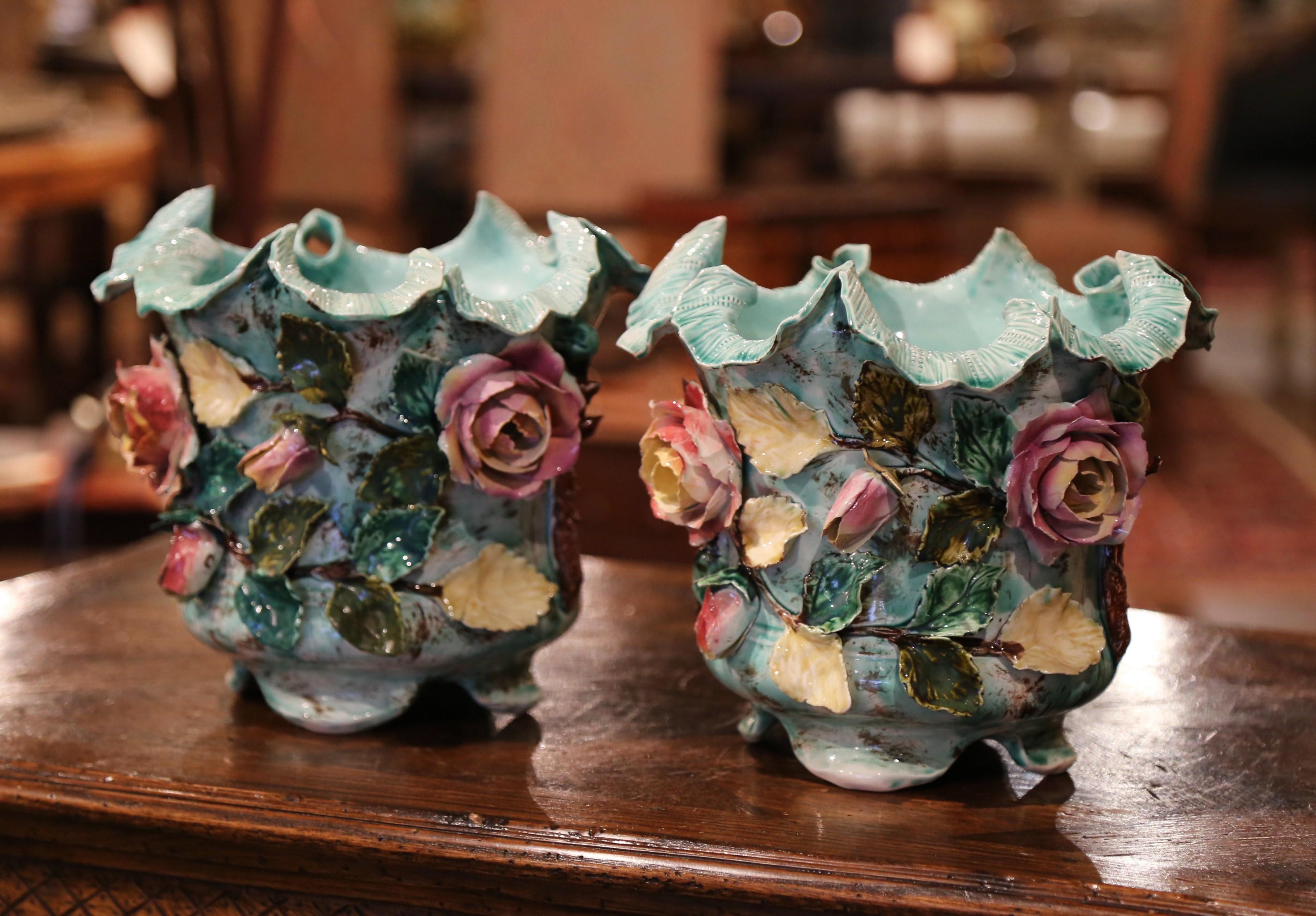 These unusual antique Majolica planters were crafted in France, circa 1870. Each decorative porcelain cache pot stands on four small scrolled feet and features colorful, high relief floral, green leaf and tree branch motifs. The colorful ceramic