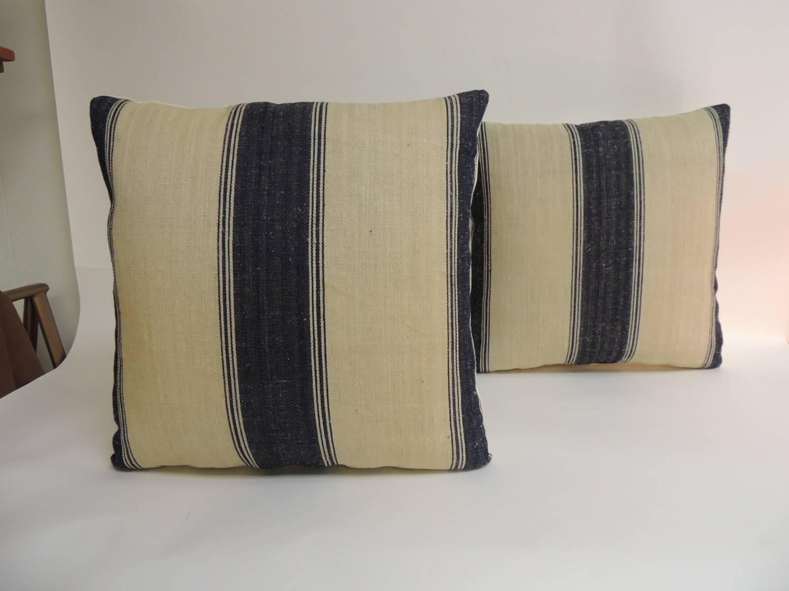 Pair of 19th century French stripes square decorative pillows in dark blue. Decorative pillows show vertical stripes on tan with a chevron woven homespun textile. French decorative cushions finalized with natural linen backings. In shades of blue,