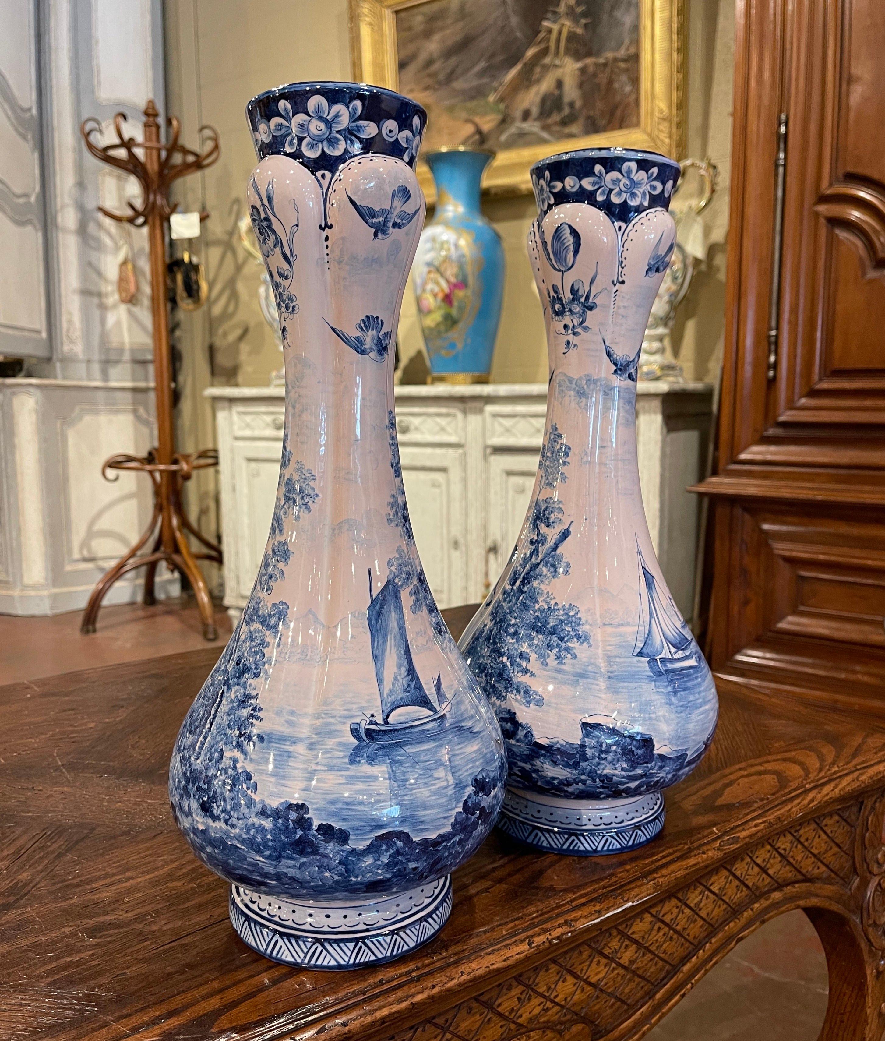 Decorate a shelf or console table with this elegant pair of antique faience vases. Crafted in France circa 1880, both vases are round in shape with a long neck over a circular mouth. Each vessel is hand painted in the traditional soft blue and white