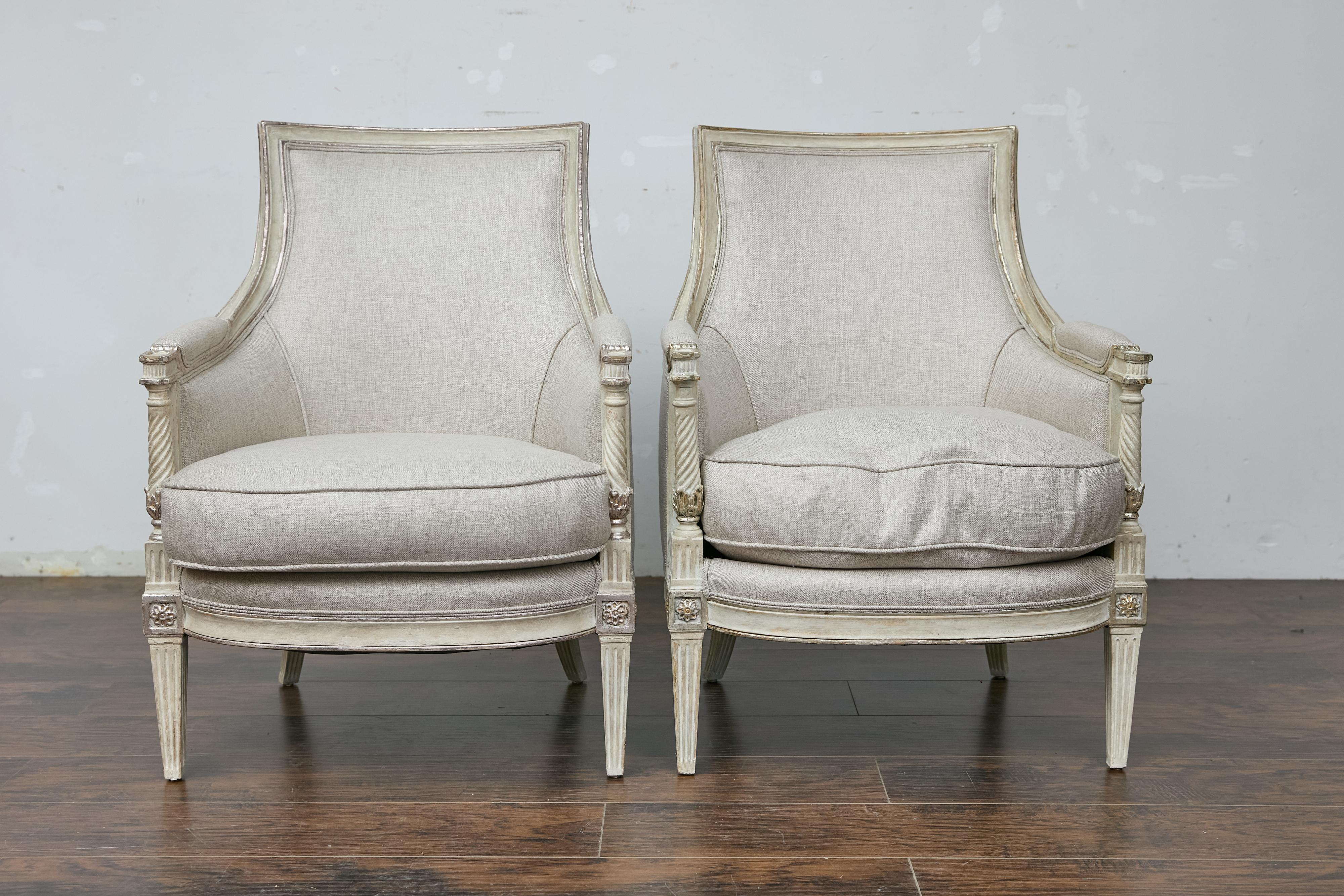 A pair of French Directoire style painted wood bergères chairs from the 19th century with twisted columns and new custom upholstery. This elegant pair of French Directoire style bergères chairs, dating back to the 19th century, exudes timeless