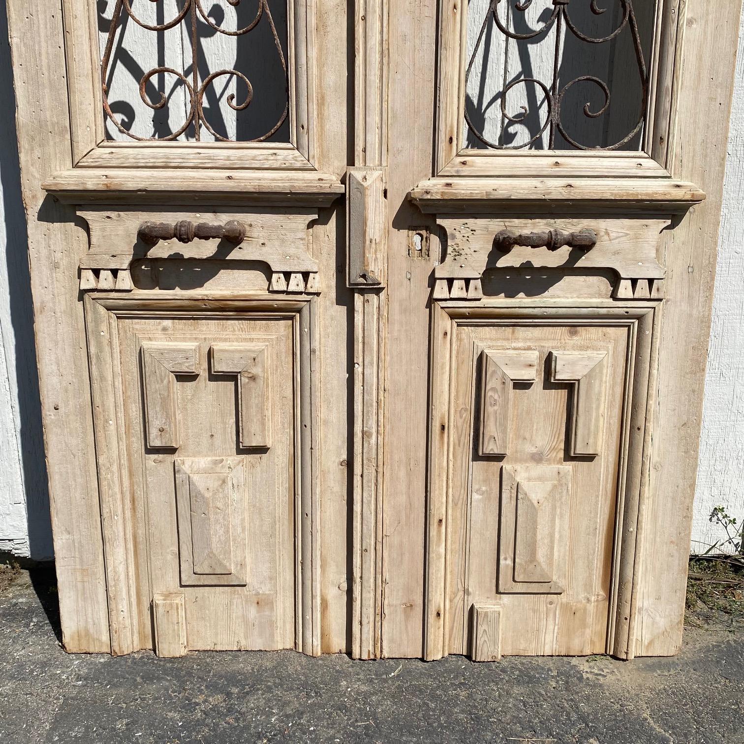 Pair of stunning stripped 19th century French doors with wrought iron, featuring bold molded detail framing the lower panels as well as the intricate wrought iron inserts above, which are artfully wrought in a beautiful geometric pattern. Original
