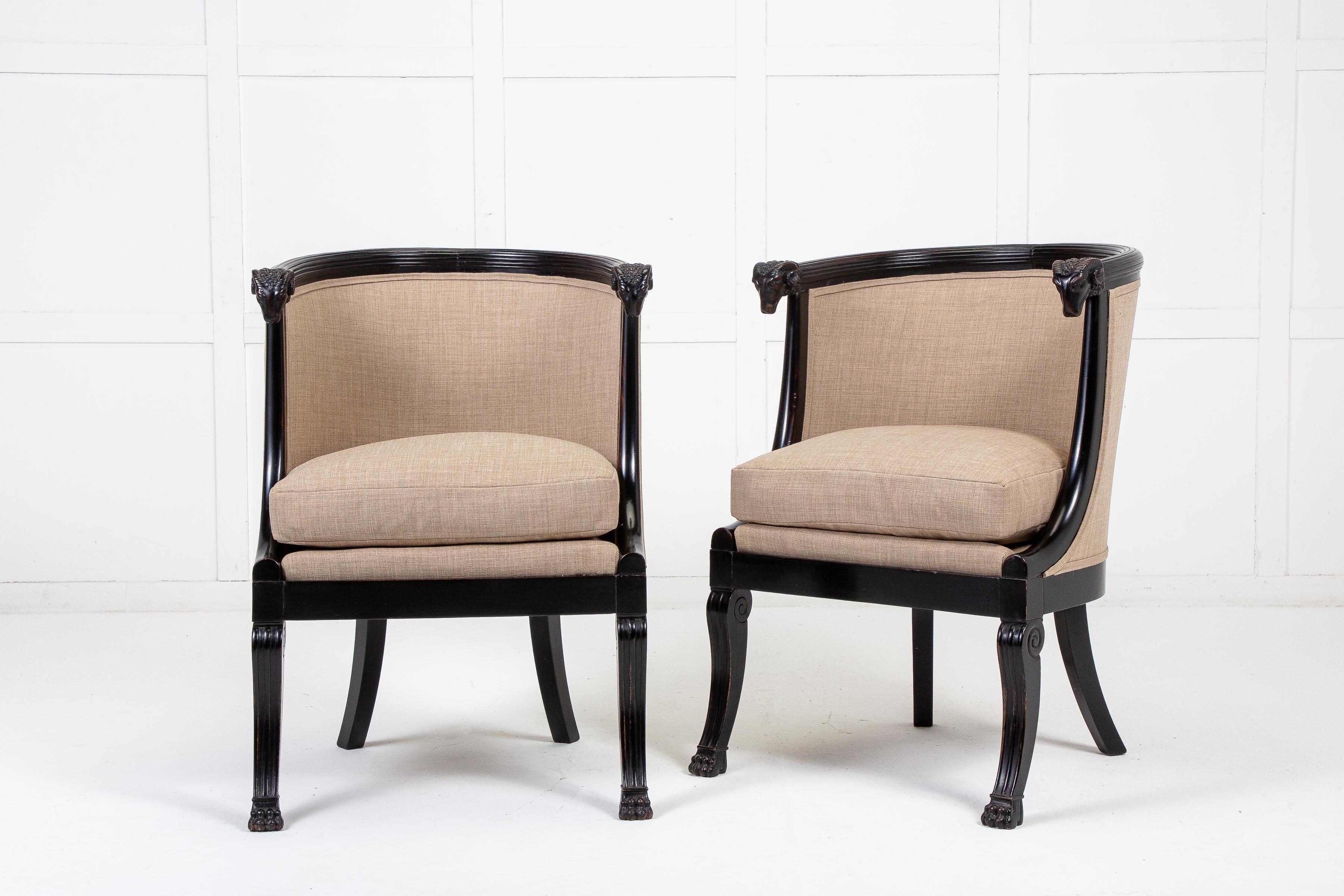 An impressive pair of 19th century French, ebonised chairs, with reeded semi circular shaped, barrel backs. Having solid carved wood frames, featuring ram's head carvings to the front supports. Deep, fully stuffed seat cushions make them