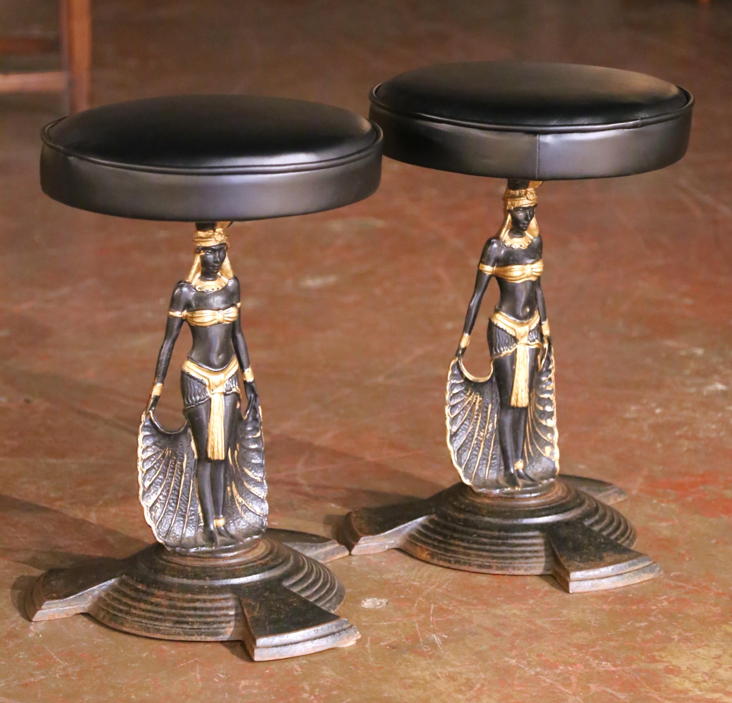 Bring sculptural elegance and historical flair to any space with this striking pair of antique stools. Crafted in France circa 1880, each stool features a cast iron base in the form of an Egyptian maiden standing atop a tiered circular plinth. The