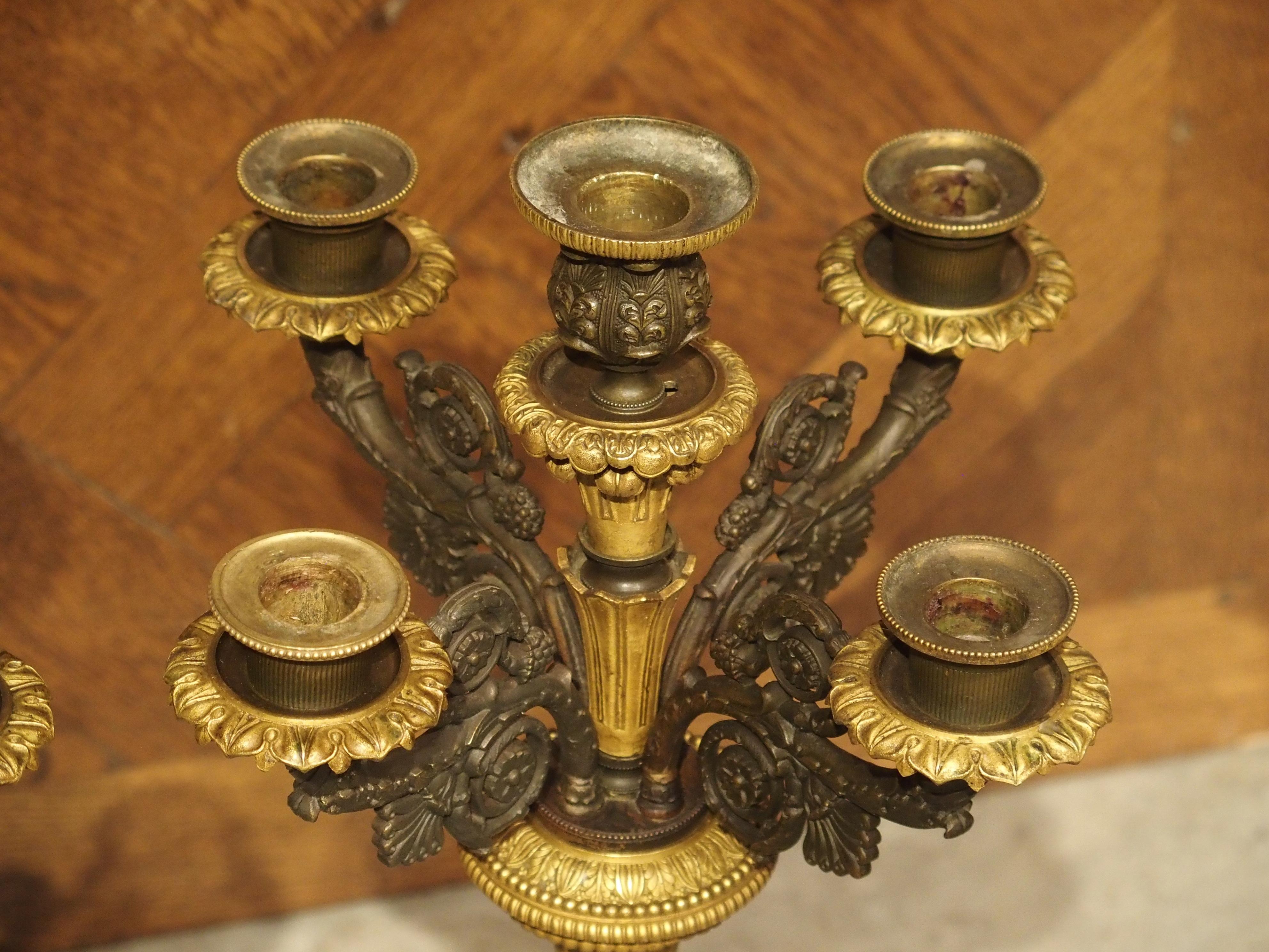 Cette paire de candélabres à cinq lumières en bronze a été produite en France au début des années 1800, pendant la période de l'Empire qui coïncide avec le règne de Napoléon. En vertu du décret de Napoléon selon lequel un roi n'est roi que