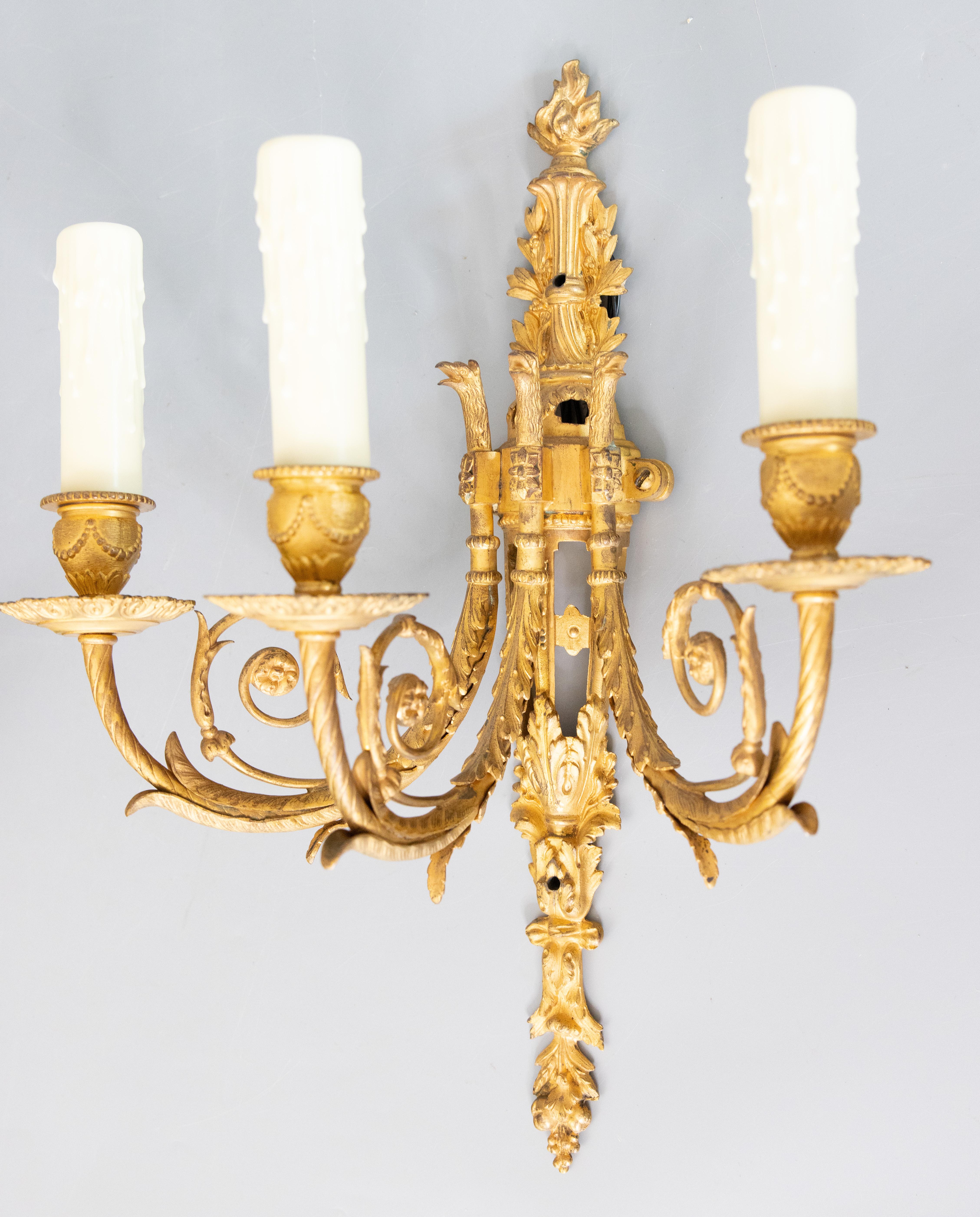 Splendida coppia di appliques a tre bracci in bronzo dorato Impero francese del XIX secolo, 1850-1870 circa. Queste bellissime appliques presentano un'incantevole patina dorata con disegni fogliacei e floreali, creature mitiche, torce e manicotti di