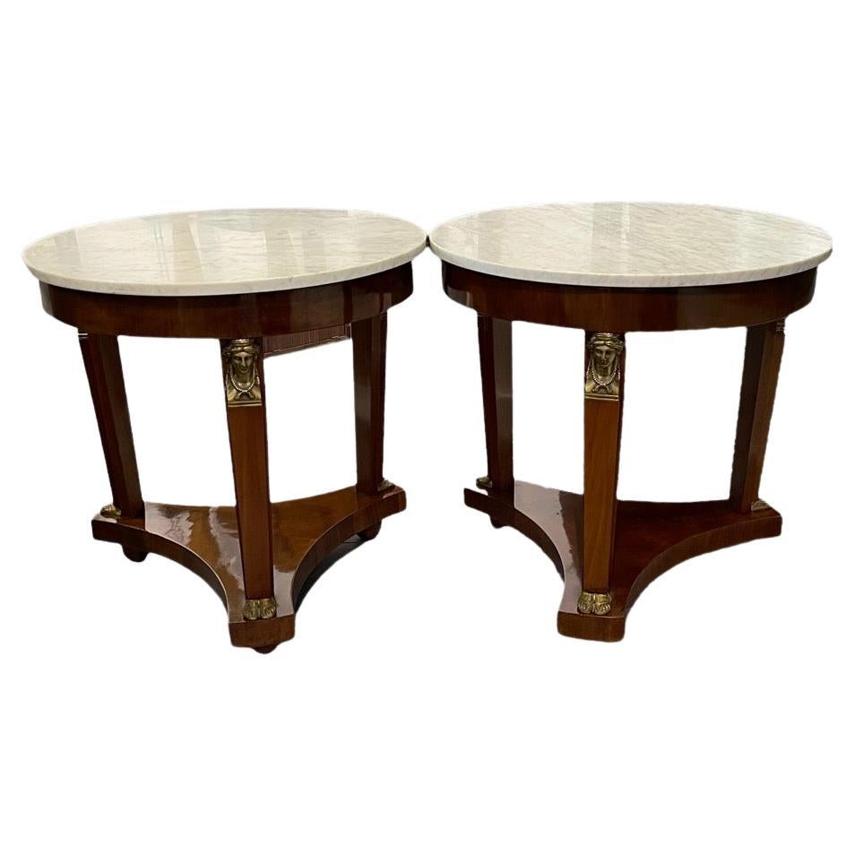 A striking pair of 19th century French Empire in the Egyptian Revival style side tables. They are characterized by a three tapered columns with bronze classical female figural masks raising a shallow apron  with Carrera marble tops. The columns rest