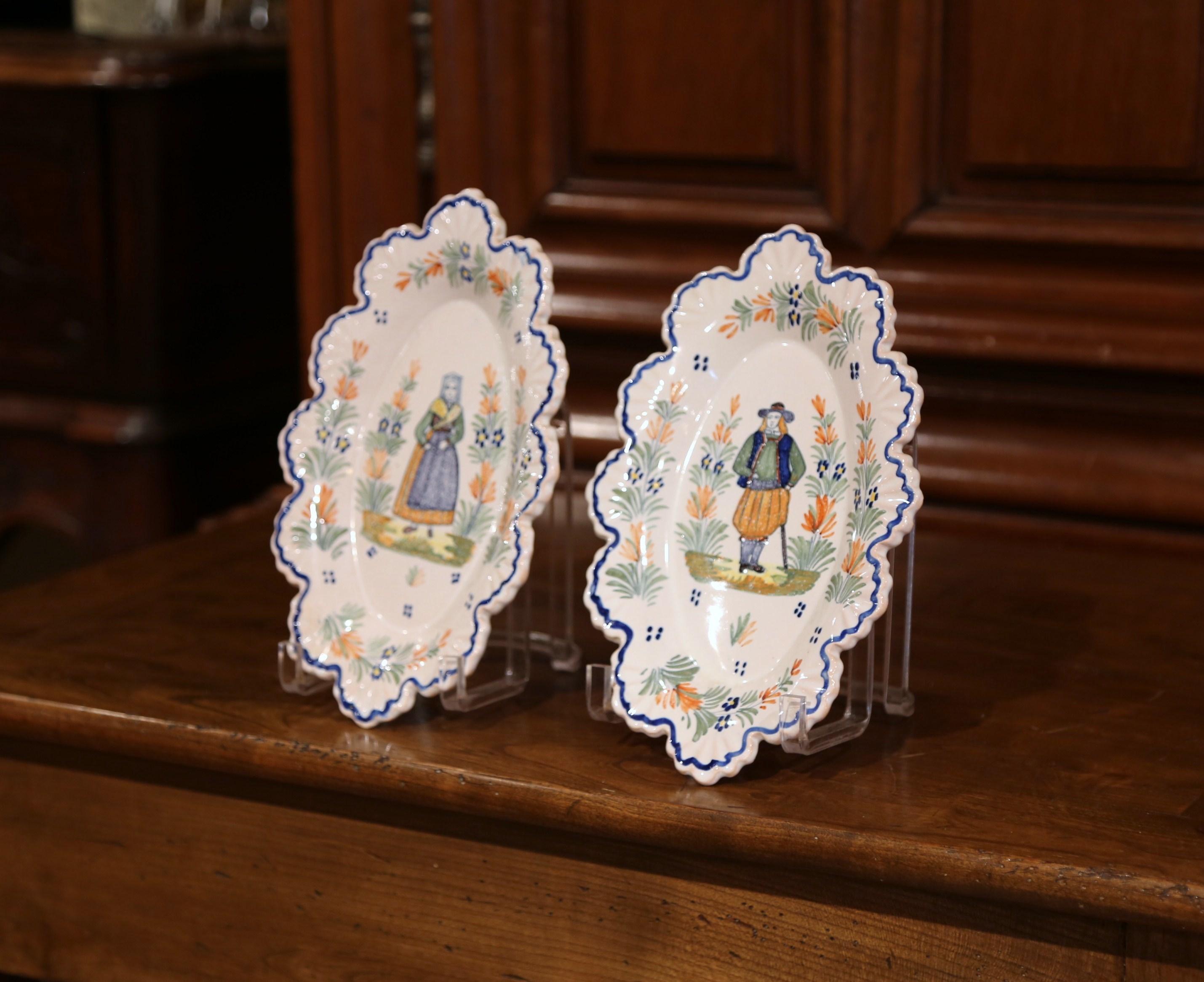 Decorate a kitchen wall or a shelf with this pair of antique decorative plates. Crafted in Brittany, circa 1890, each faience plate is hand painted with traditional Breton figure motifs, and is further embellished with floral decor. Both platters