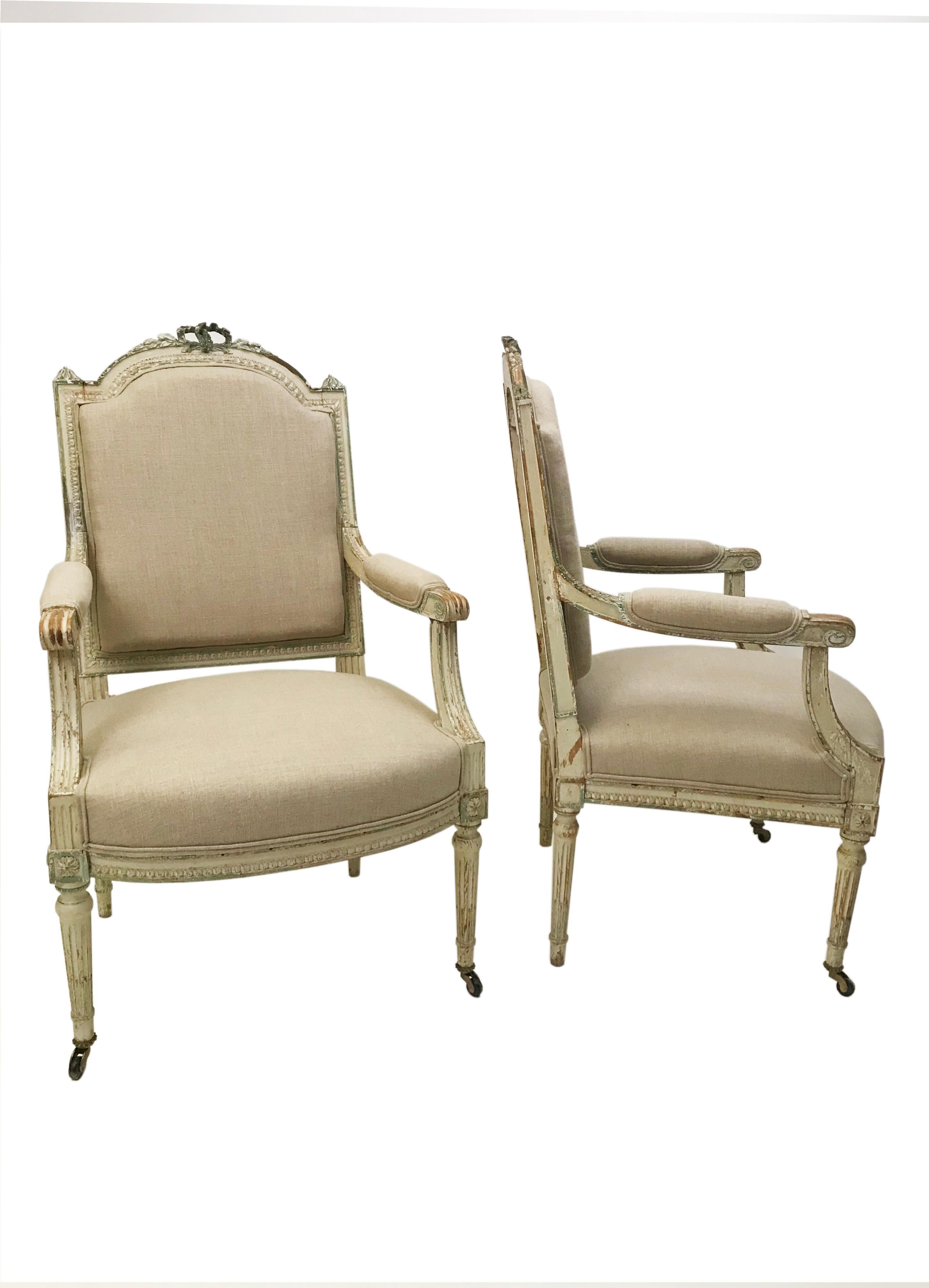 Pair of French painted fauteils armchairs, 19th century. Hand carved in the classical style and hand painted with original finish in soft cream and green. Frames are walnut, in the style of Louis XVI. Decorative Ribbon carved crest. Upholstered in a